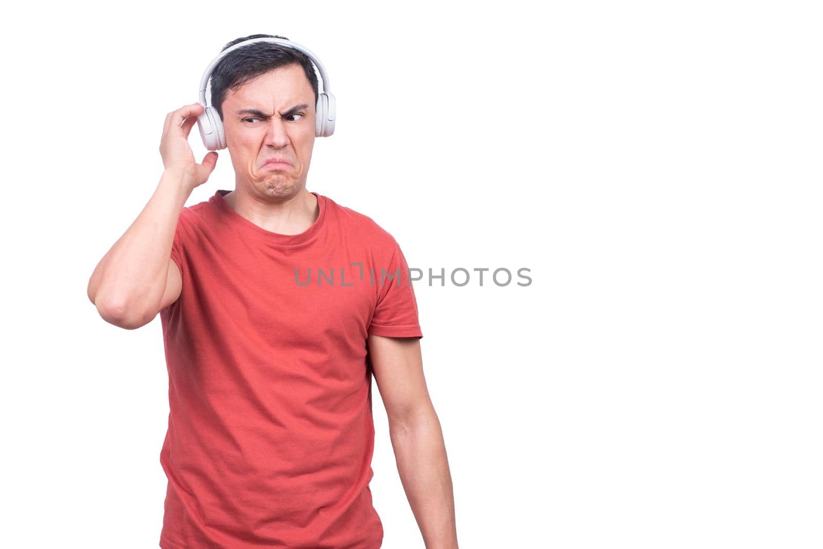 Isolated male model in red t shirt touching headphones unsatisfied with music on white backdrop