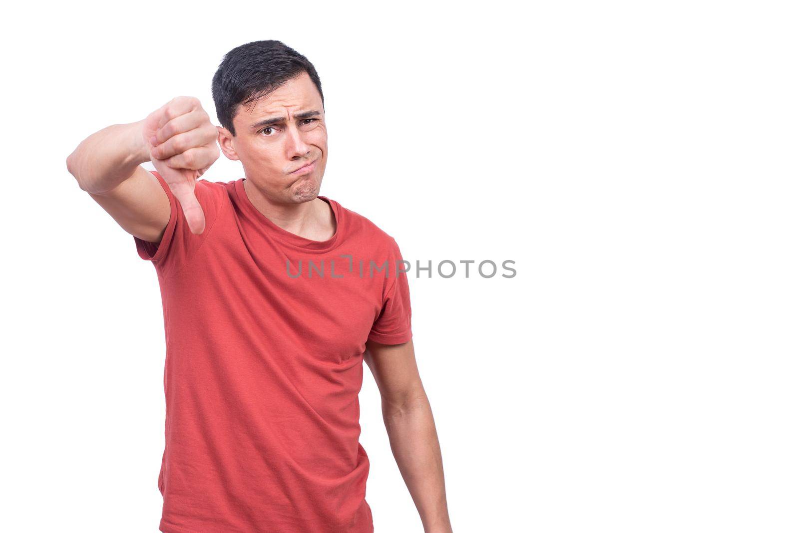 Brunet in casual clothes looking at camera while standing on white background with thumb down
