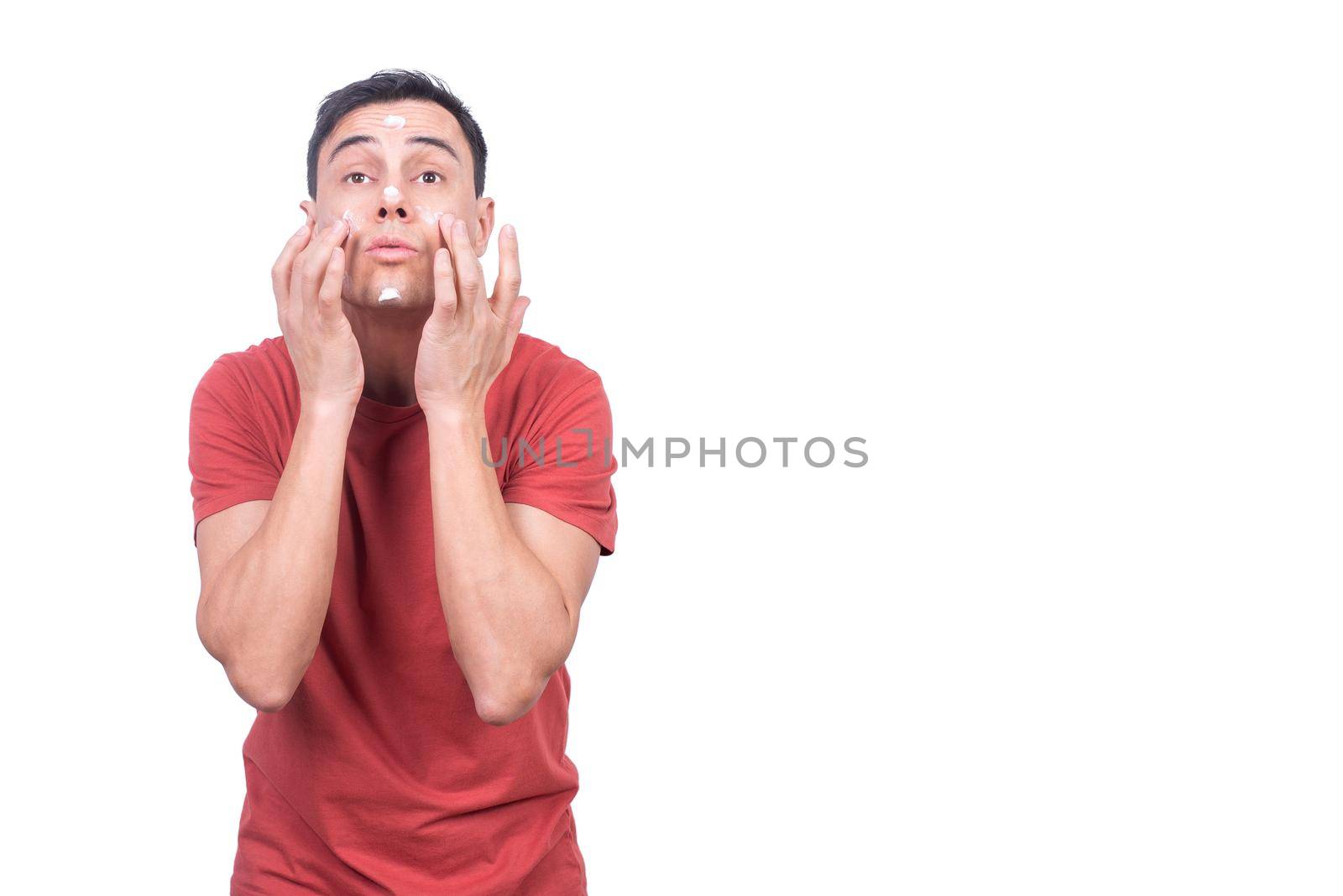 Man in t shirt applying anti aging facial cream on face during daily skincare routine isolated on white background in studio