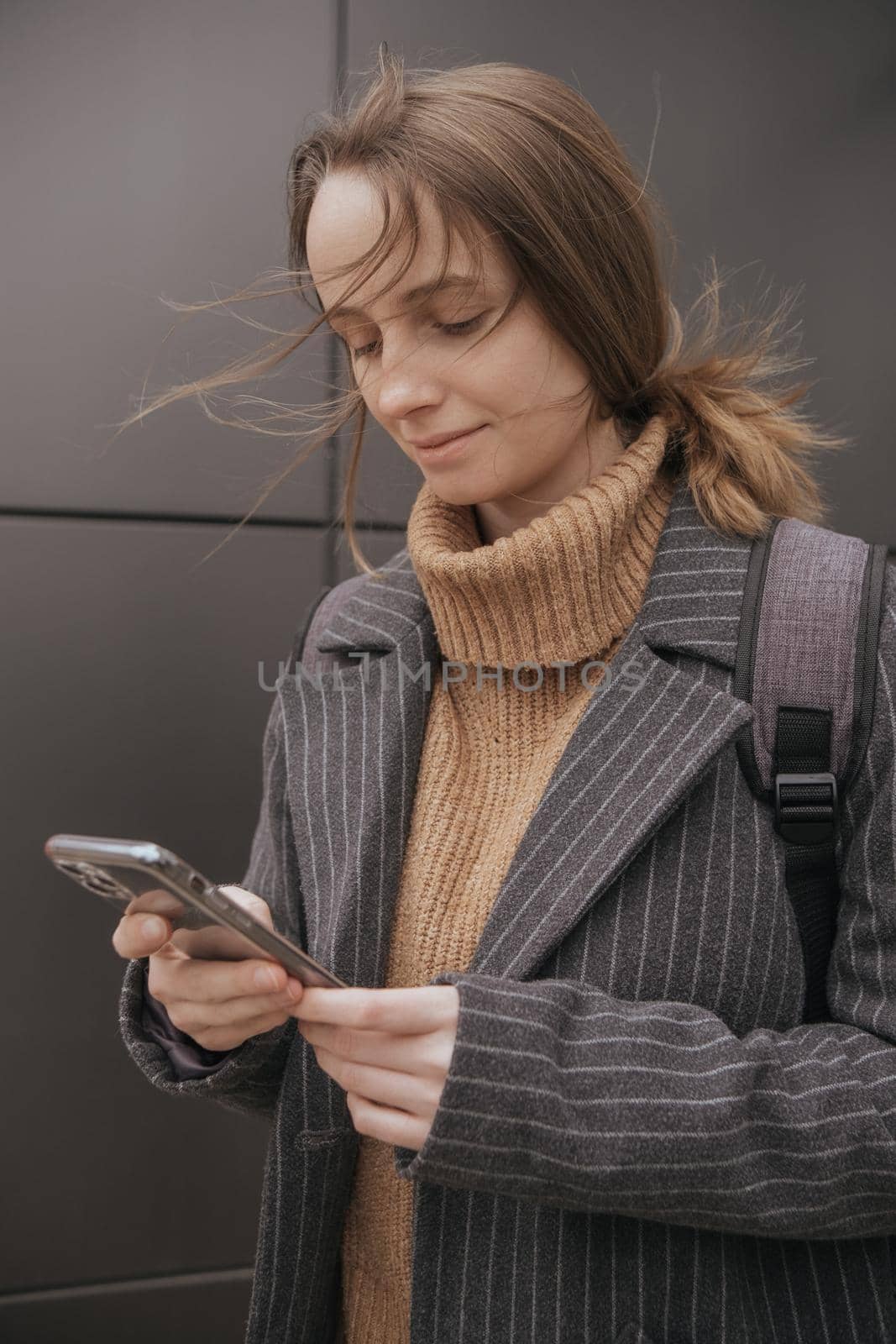 Portrait of happy hipster woman typing by mobile phone outdoors. Closeup cheerful girl walking with smartphone in urban background. Smiling lady holding cellphone in hands outside.
