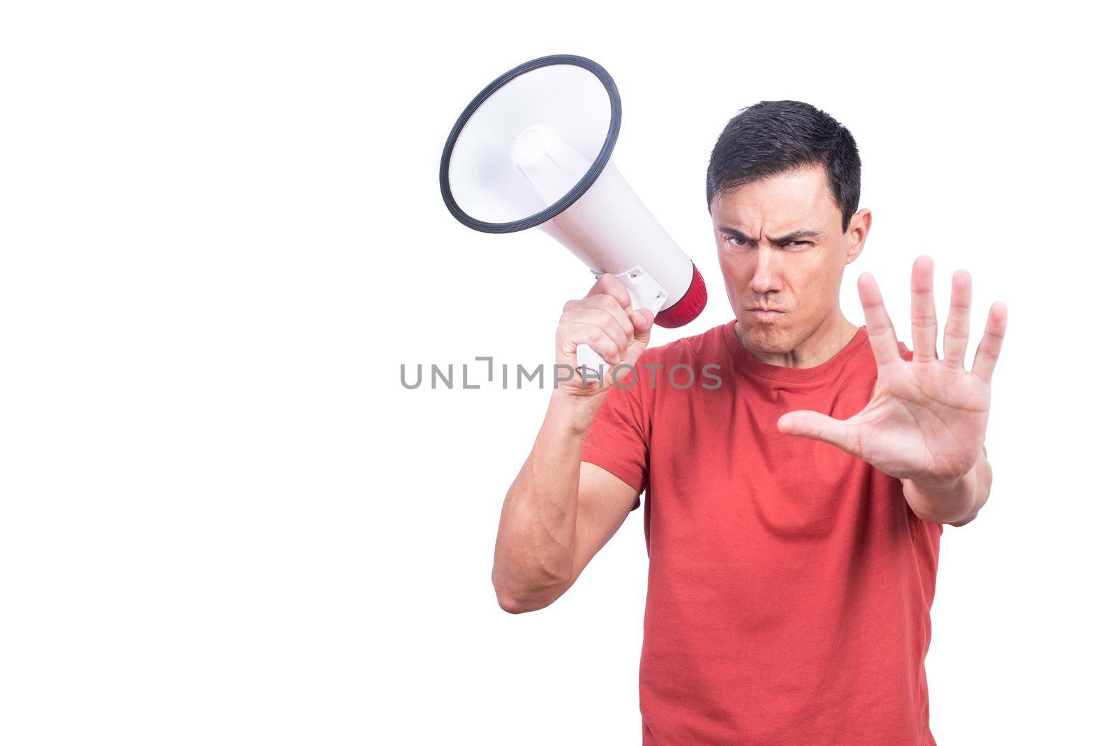 Guy showing stop gesture and looking at camera while standing with loudspeaker on white background in studio