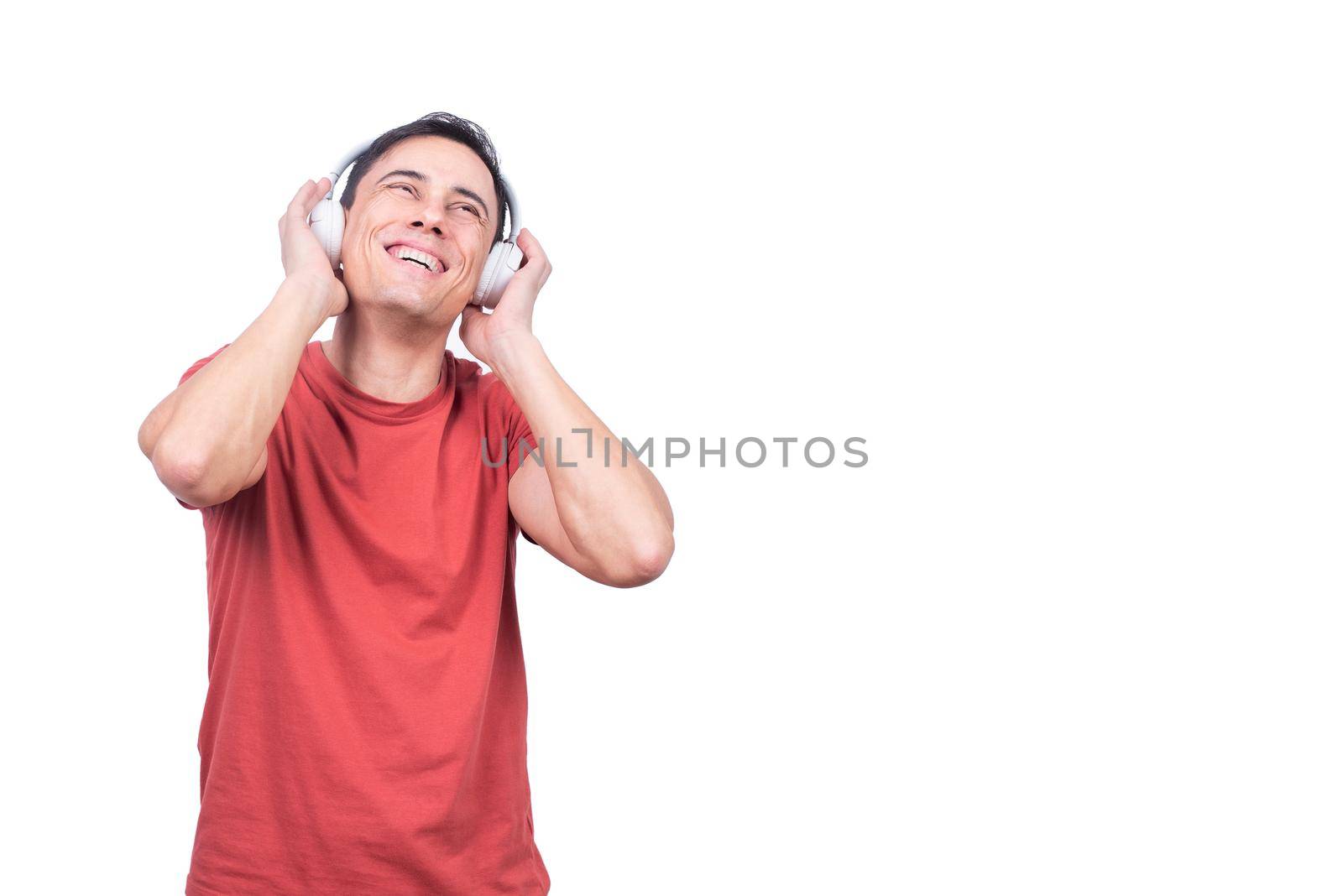 Positive guy in casual clothes enjoying music in wireless headphones while standing on white background in studio