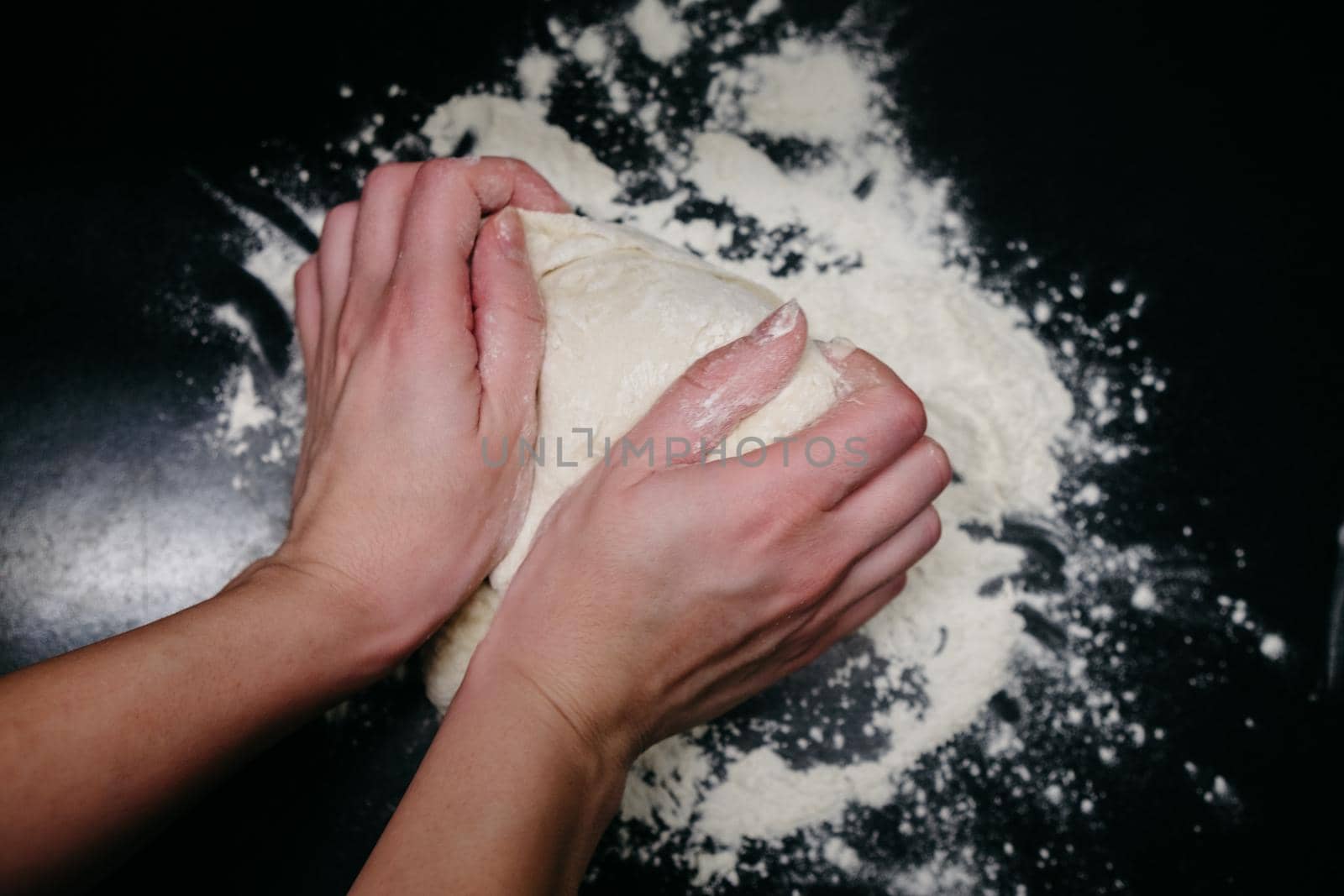 Pizza dough on a black table with hands and light