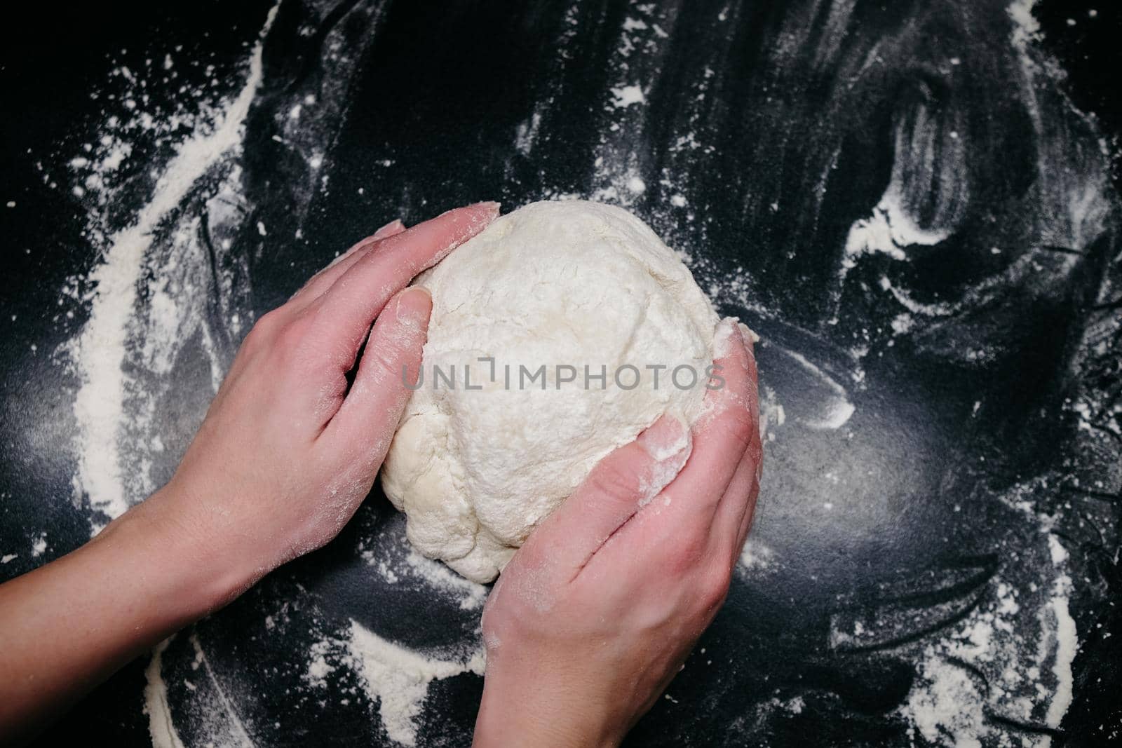 Pizza dough on a black table with hands and light