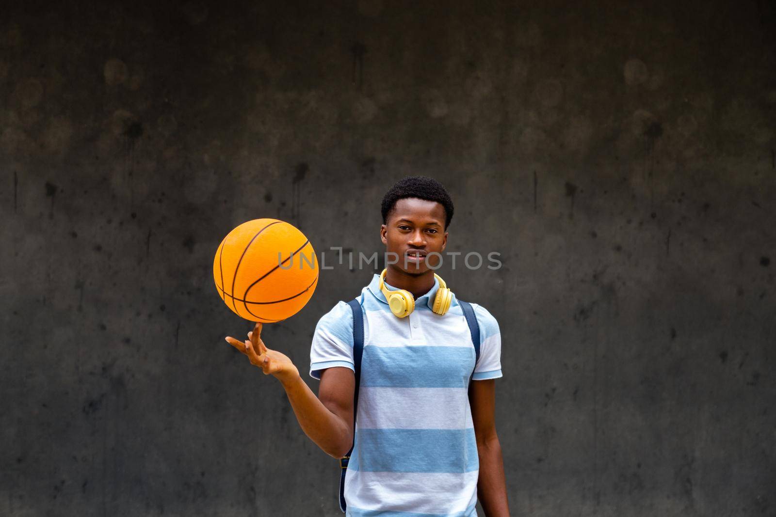 Teen African American boy spinning basketball ball on finger looking at camera. Copy space. Sports concept.