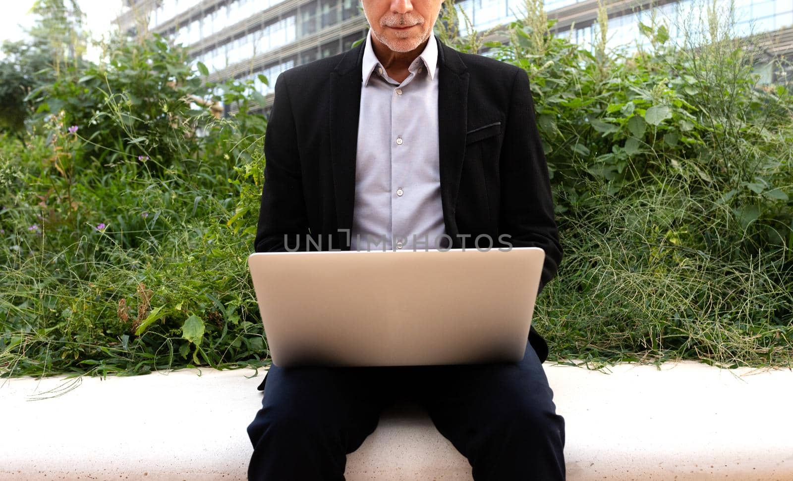 Unrecognisable caucasian business man working outdoors using laptop. by Hoverstock