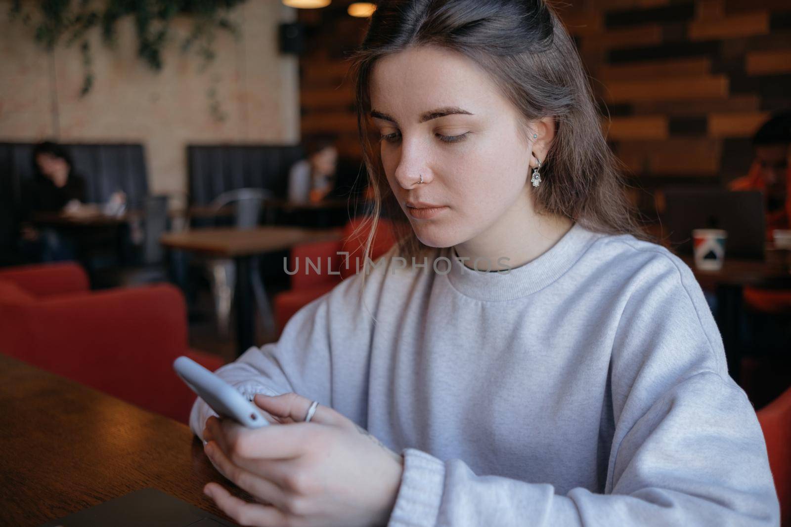 Happy smiling gorgeous woman in fashionable glasses reading pleasant text message on mobile phone while sitting in coffee shop during recreation time. by Symonenko