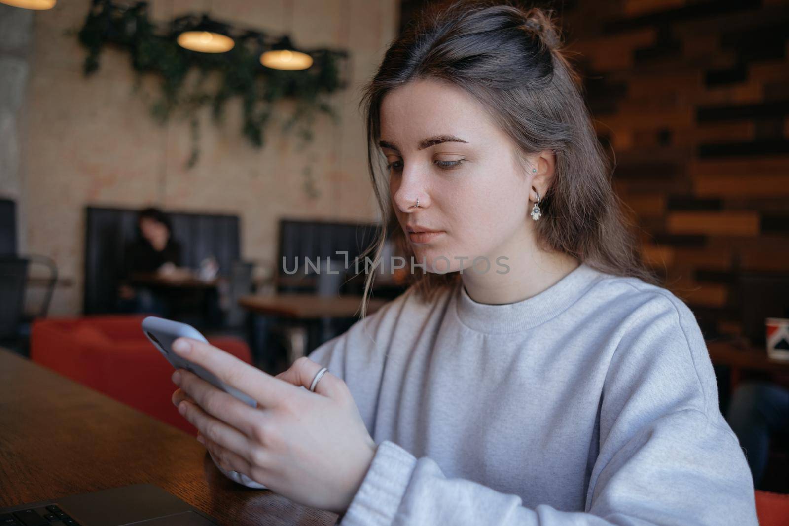 Happy smiling gorgeous woman in fashionable glasses reading pleasant text message on mobile phone while sitting in coffee shop during recreation time. by Symonenko