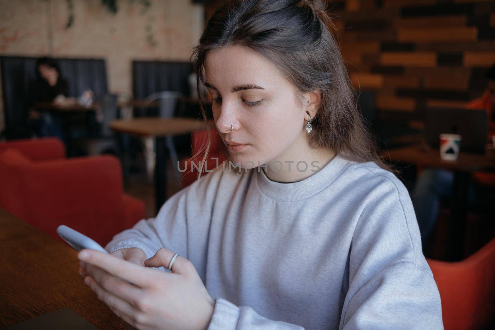 Happy smiling gorgeous woman in fashionable glasses reading pleasant text message on mobile phone while sitting in coffee shop during recreation time. Joyful female watching video on cellphone