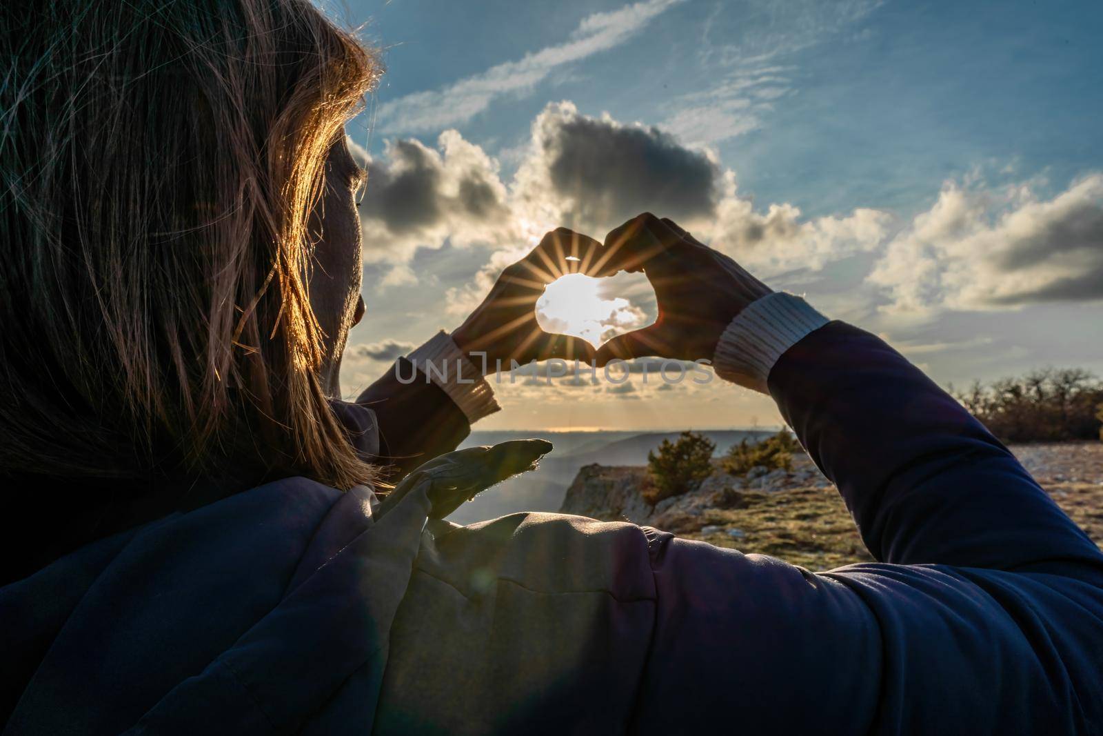 The girl made a beautiful heart from her finger in the rays of the sun. healthy woman making heart shape with hands at sunset. Shining summer sun on your hands. healthy heart concept. by Matiunina