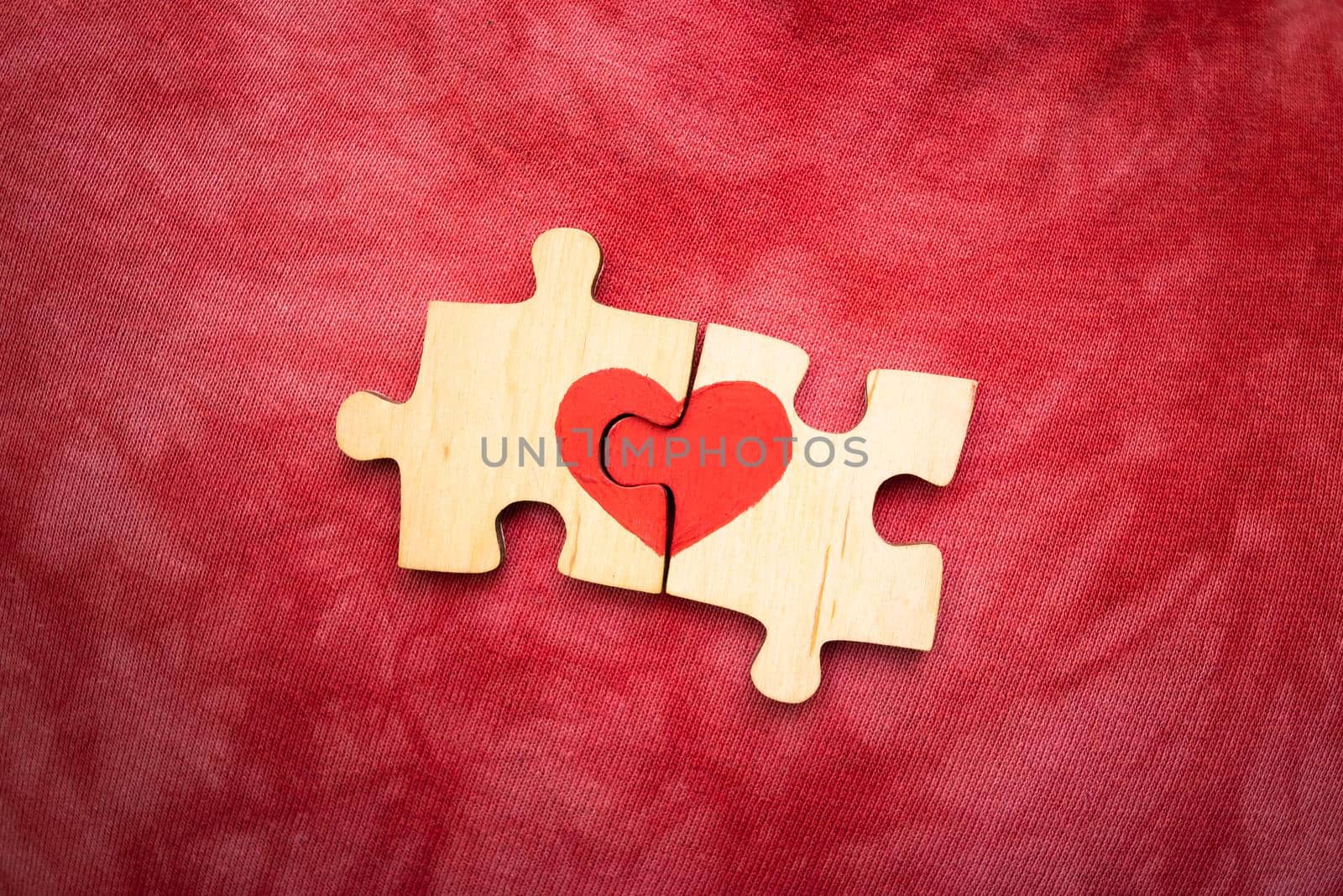 Red heart is drawn on the pieces of the wooden puzzle lying next to each other on red background. Love concept. St. Valentine day.