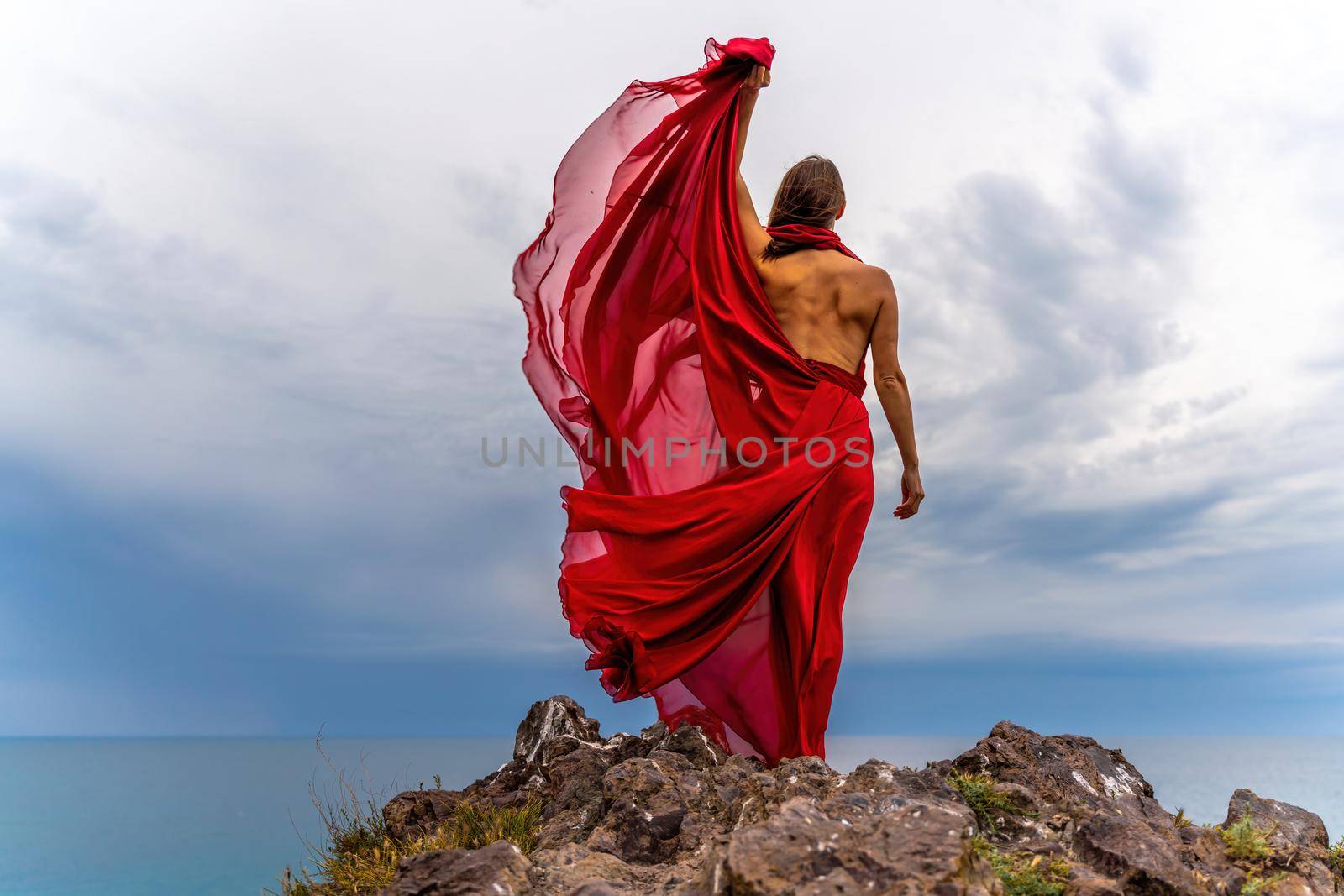 Woman in red dress dance over storm sky, gown fluttering fabric flying as splash.