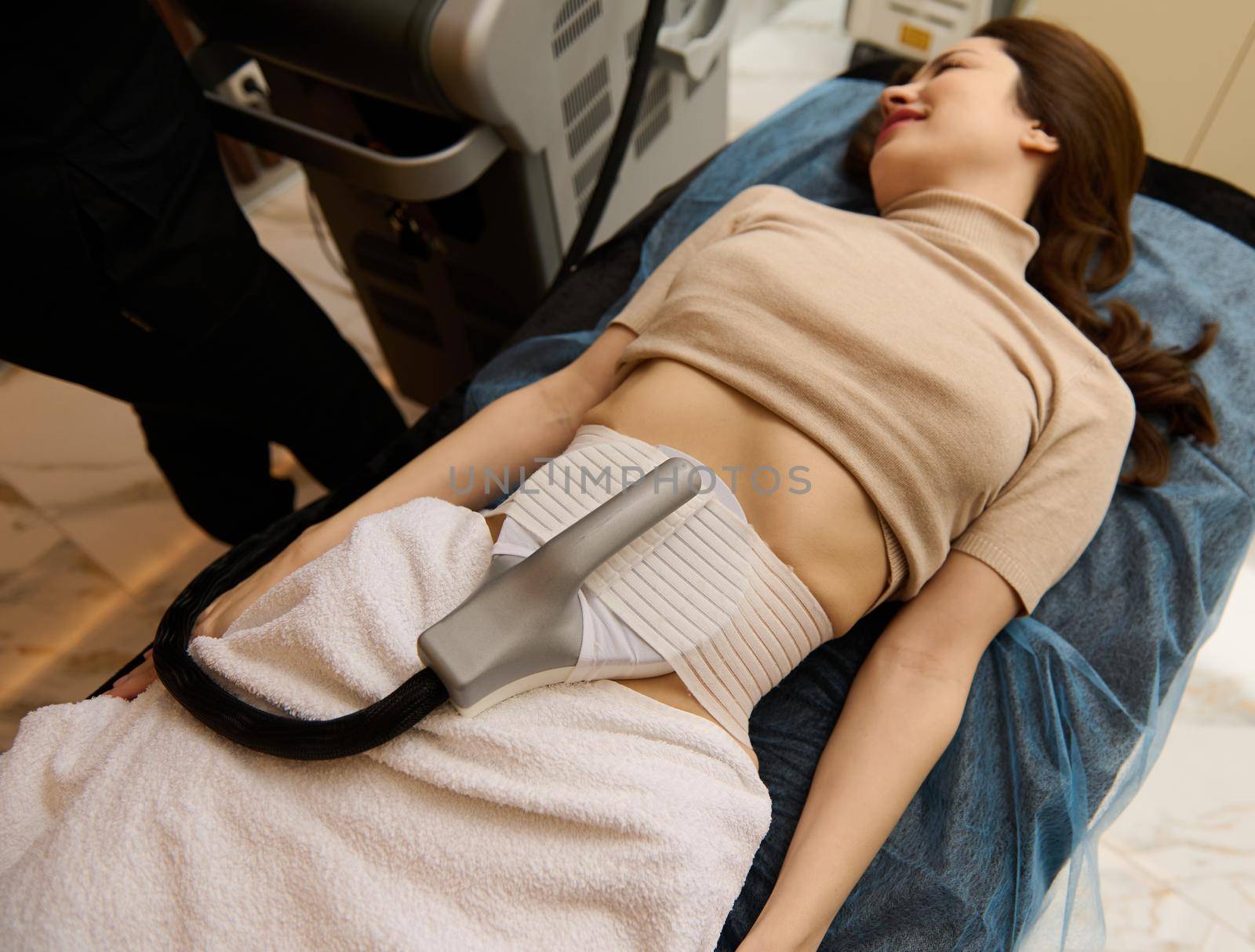 Beautiful Caucasian brunette receiving lipo laser therapy, anti-cellulite treatment in medical spa. Cosmetic fat reduce treatment. Non surgical body sculpting and body contouring