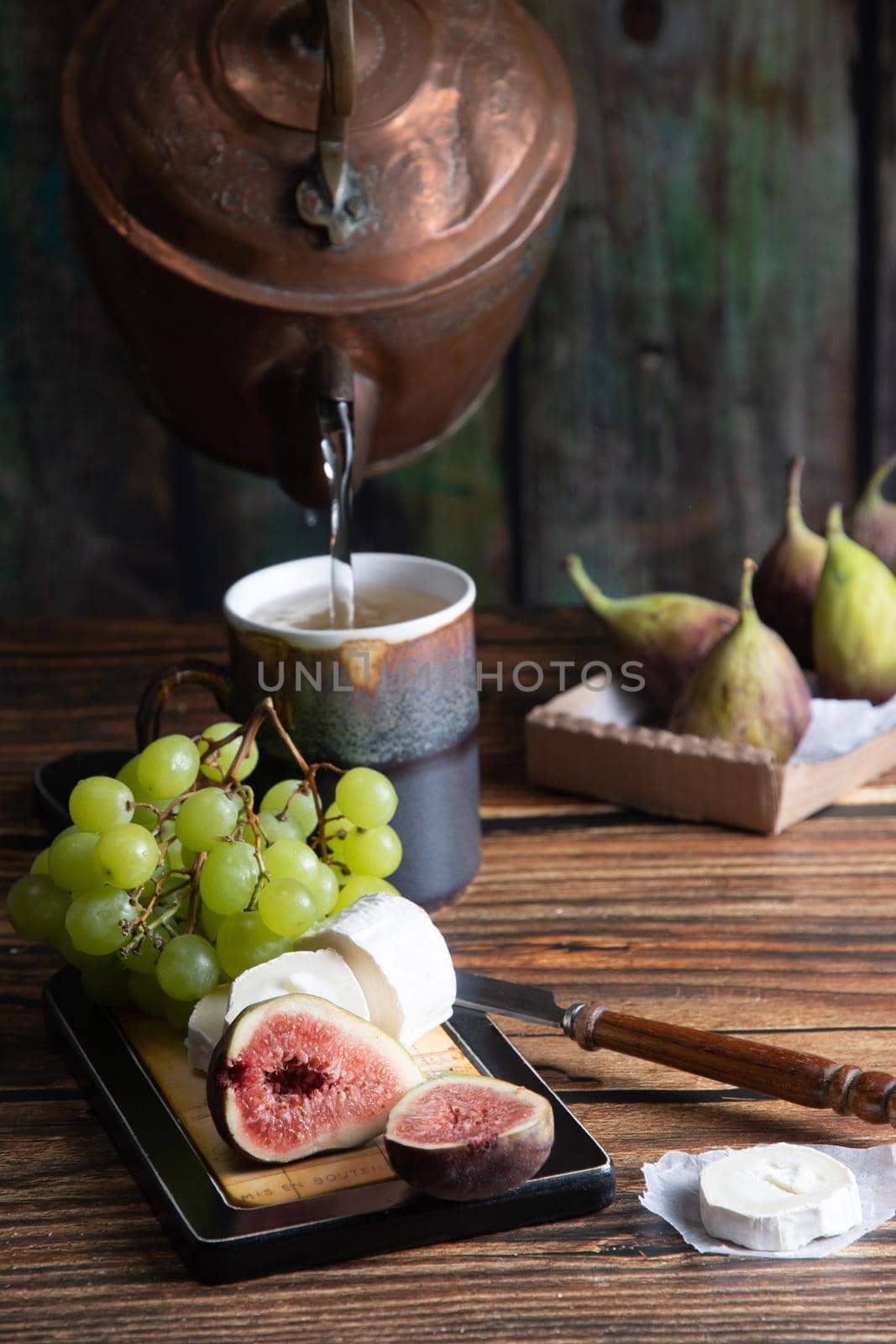 cheese plate with goat cheese, grapes and figs, copper teapot, angle view, healthy food, high-calorie breakfast. High quality photo