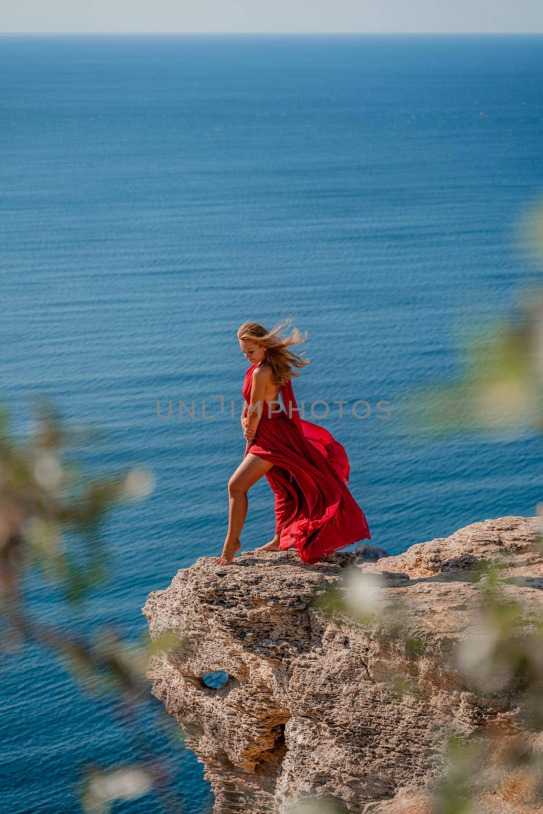 A woman in a red flying dress fluttering in the wind, against the backdrop of the sea. by Matiunina