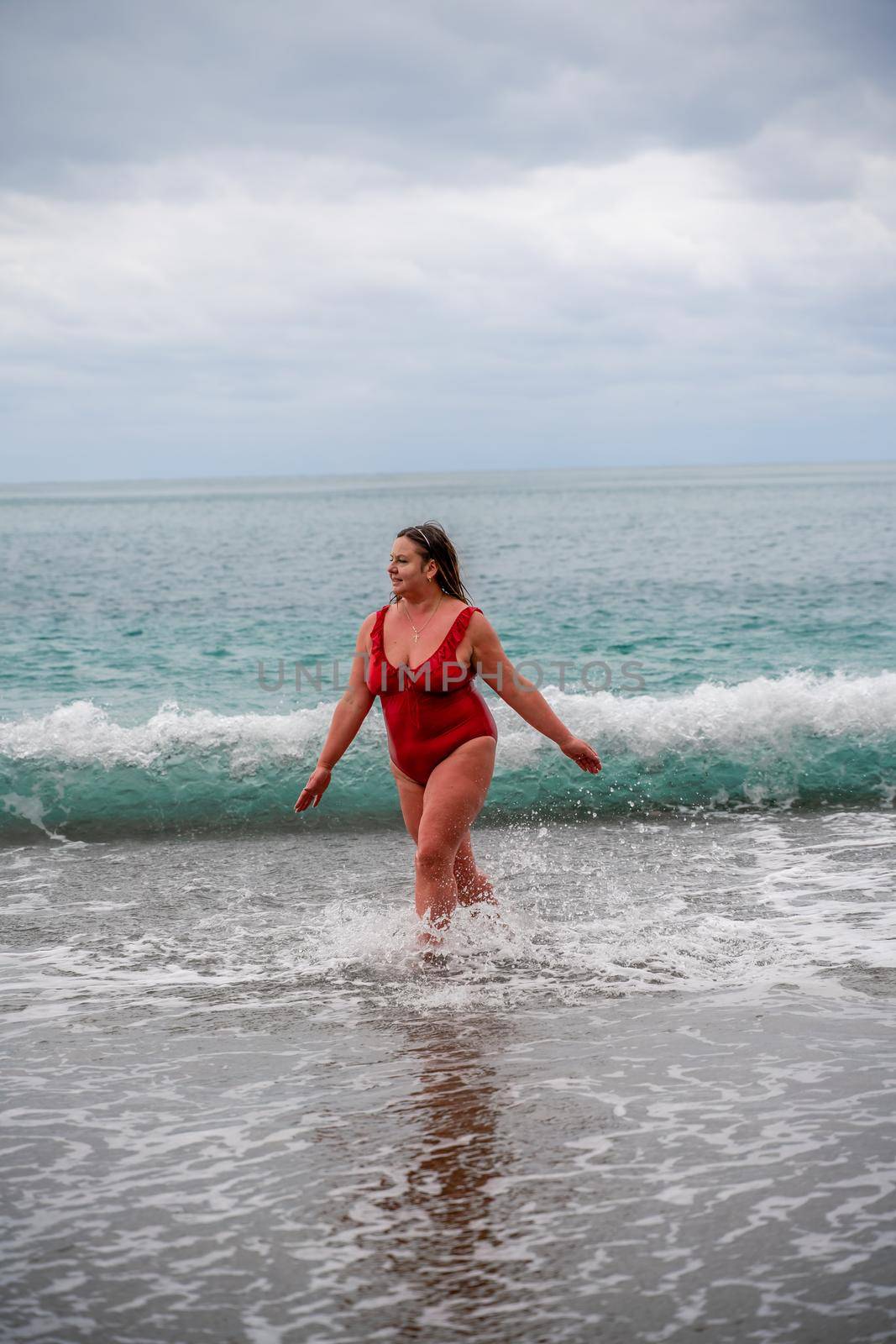 Woman in a bathing suit at the sea. A fat young woman in a red swimsuit enters the water during the surf by Matiunina