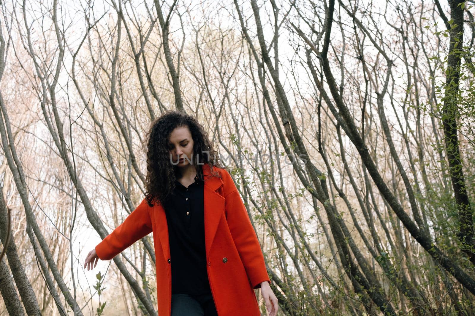 portrait of curly brunette woman in red coat in the park by Symonenko