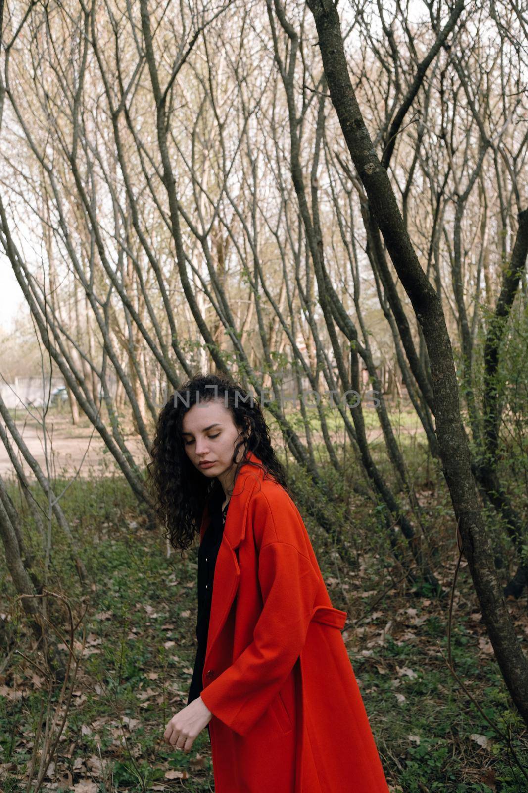 portrait of curly brunette woman in red coat in the park by Symonenko