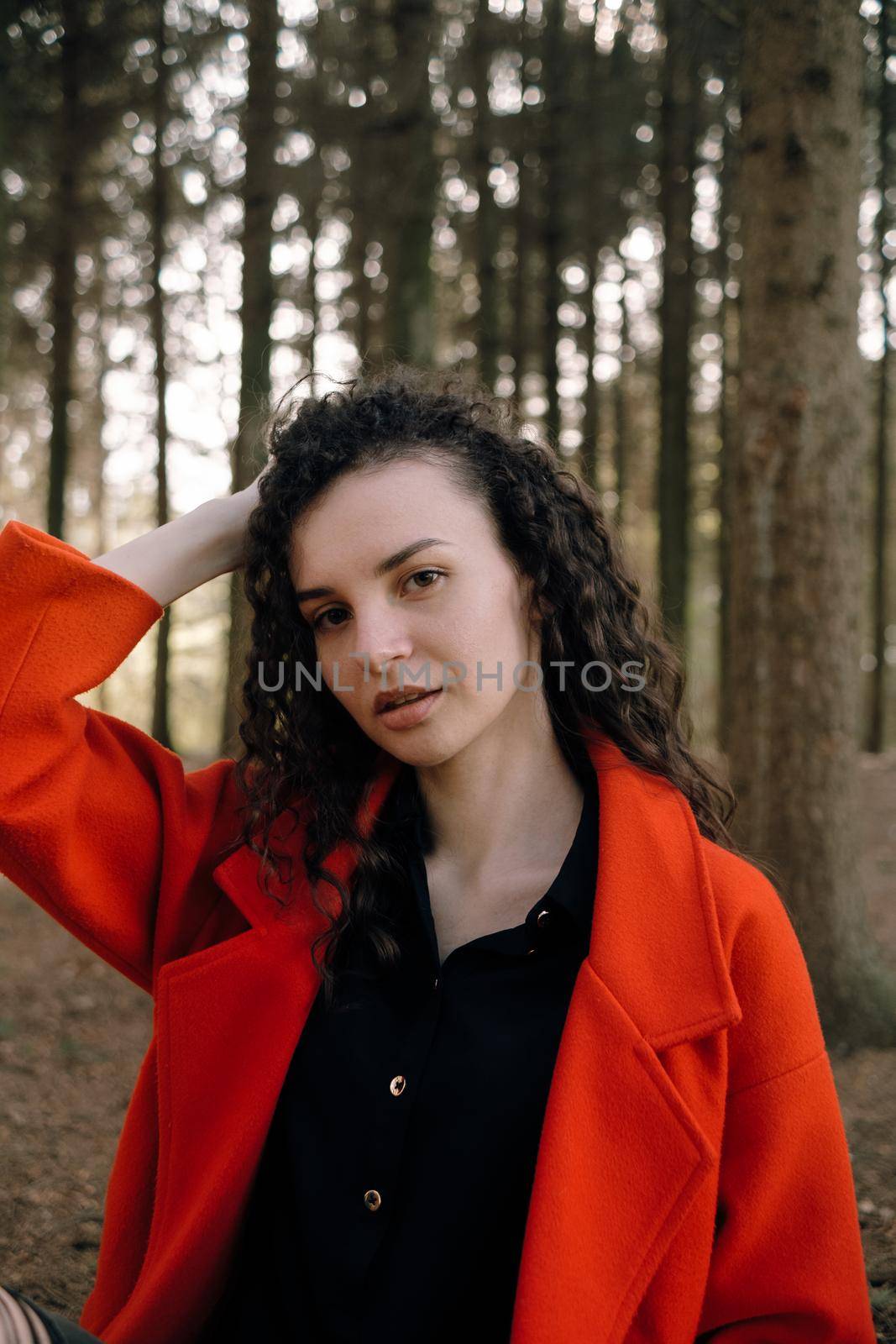 portrait of curly brunette woman in red coat in the park by Symonenko