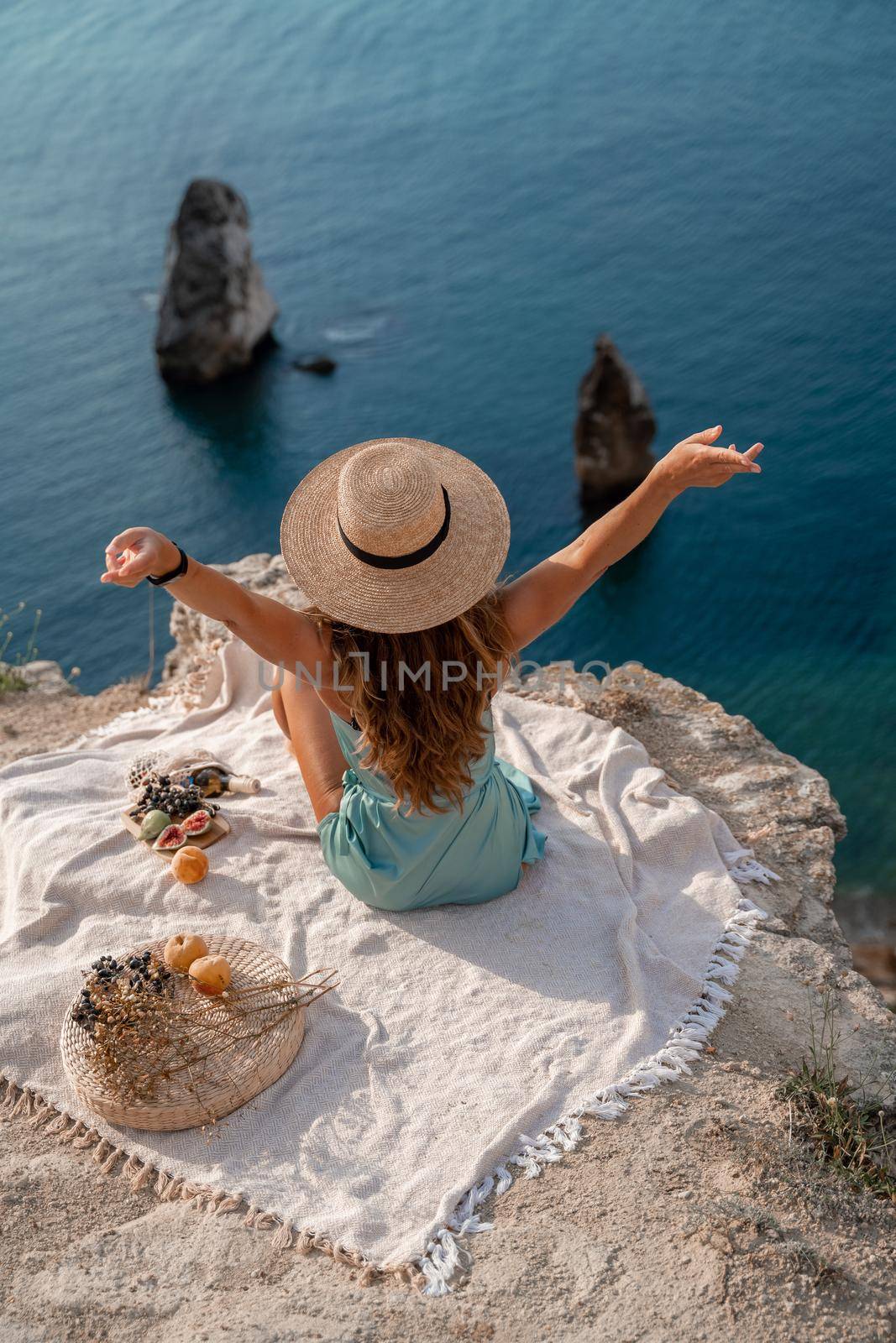 Street photo of a beautiful woman with dark hair in a mint dress and hat having a picnic on a hill overlooking the sea