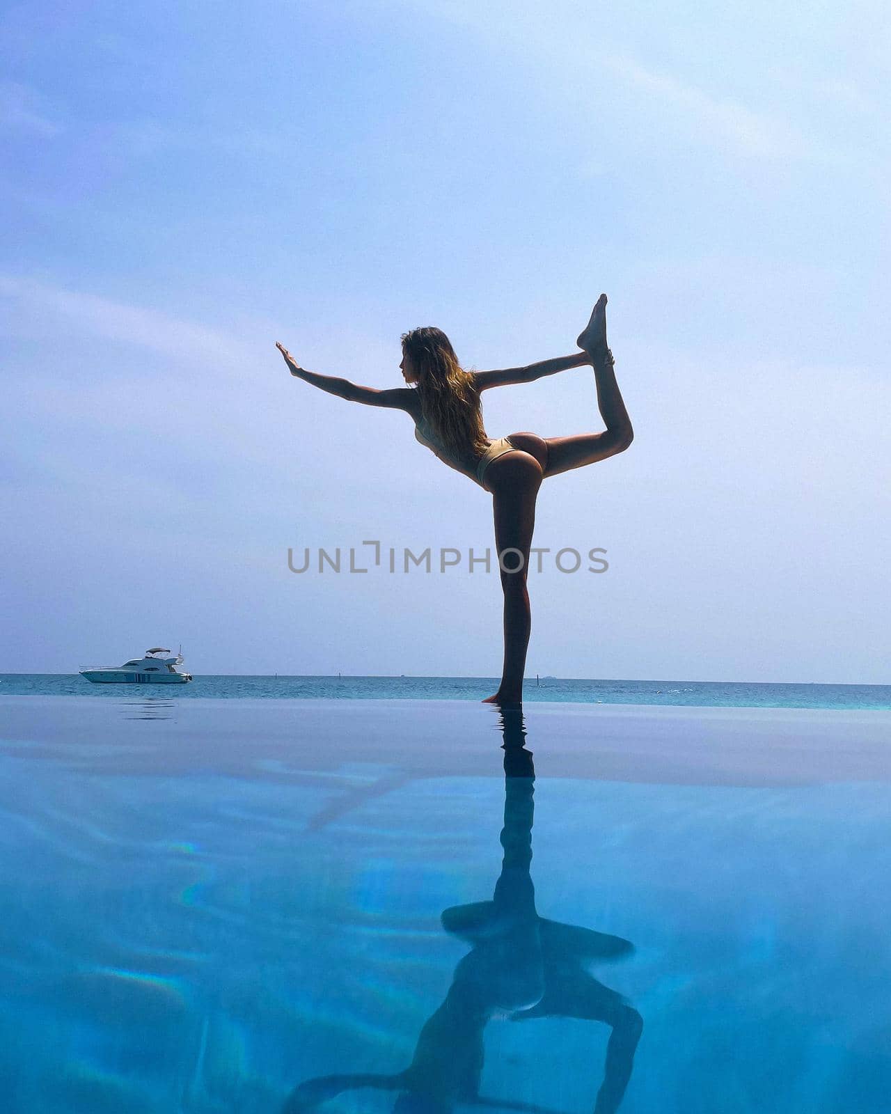 Beautiful slender woman in a swimsuit practicing yoga, Maldives, beautiful background, clean water, pool, sea and ocean.