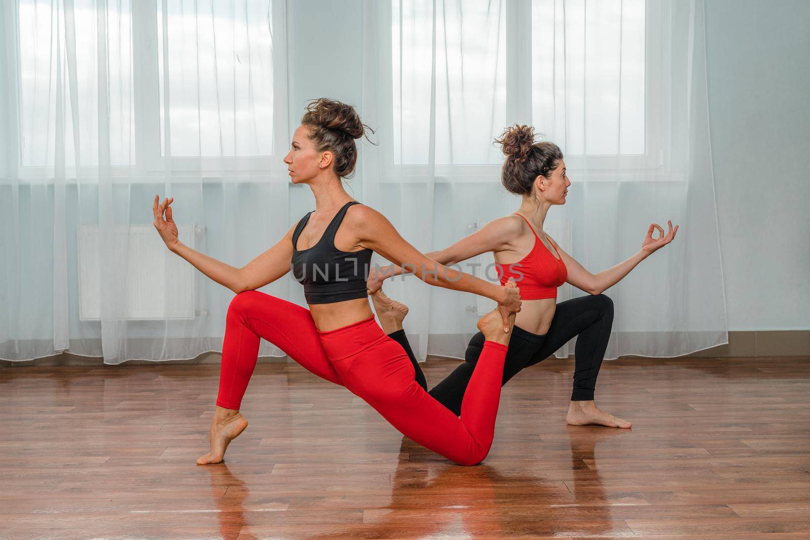Two attractive athletic girls train asana yoga pose in red jumpsuits in the gym. A group of young women stretch out in the gym. Healthy lifestyle Concept by Matiunina