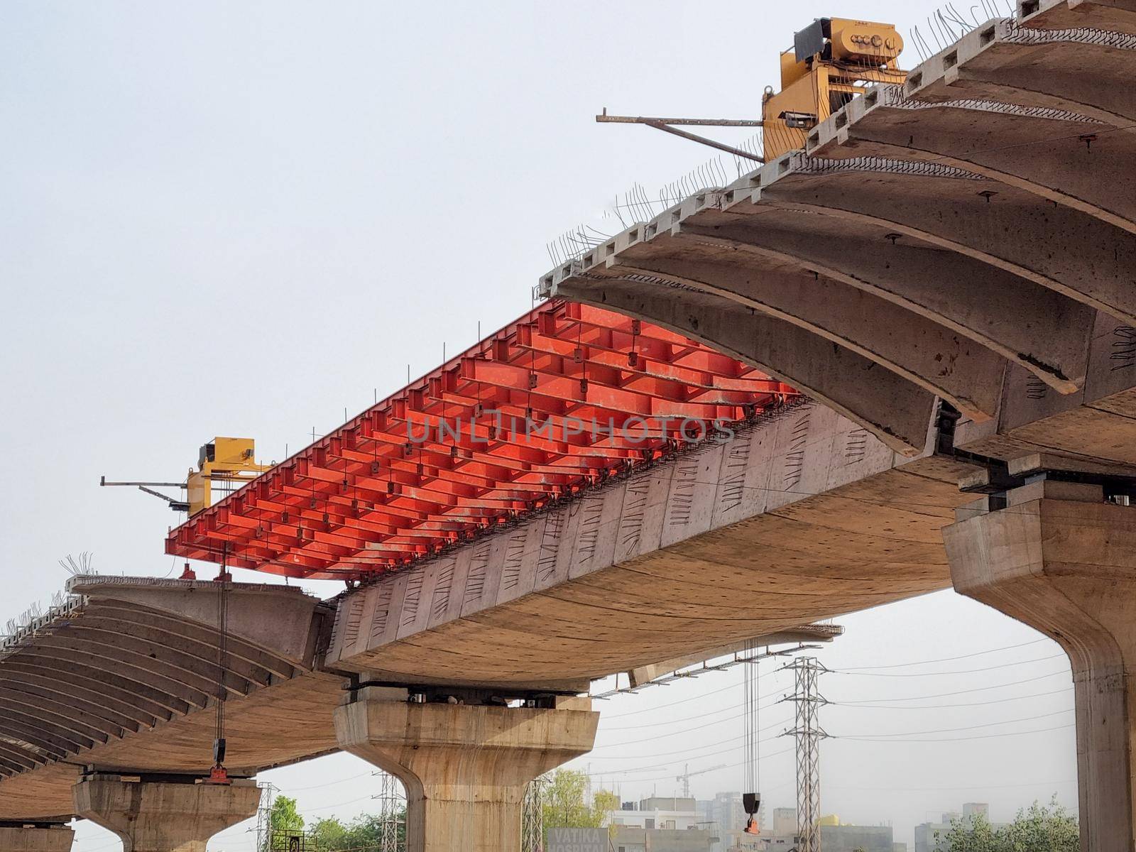 under construction bridge with red supports placed for metro train tracks, expressway to help solve traffic problem of delhi India by Shalinimathur