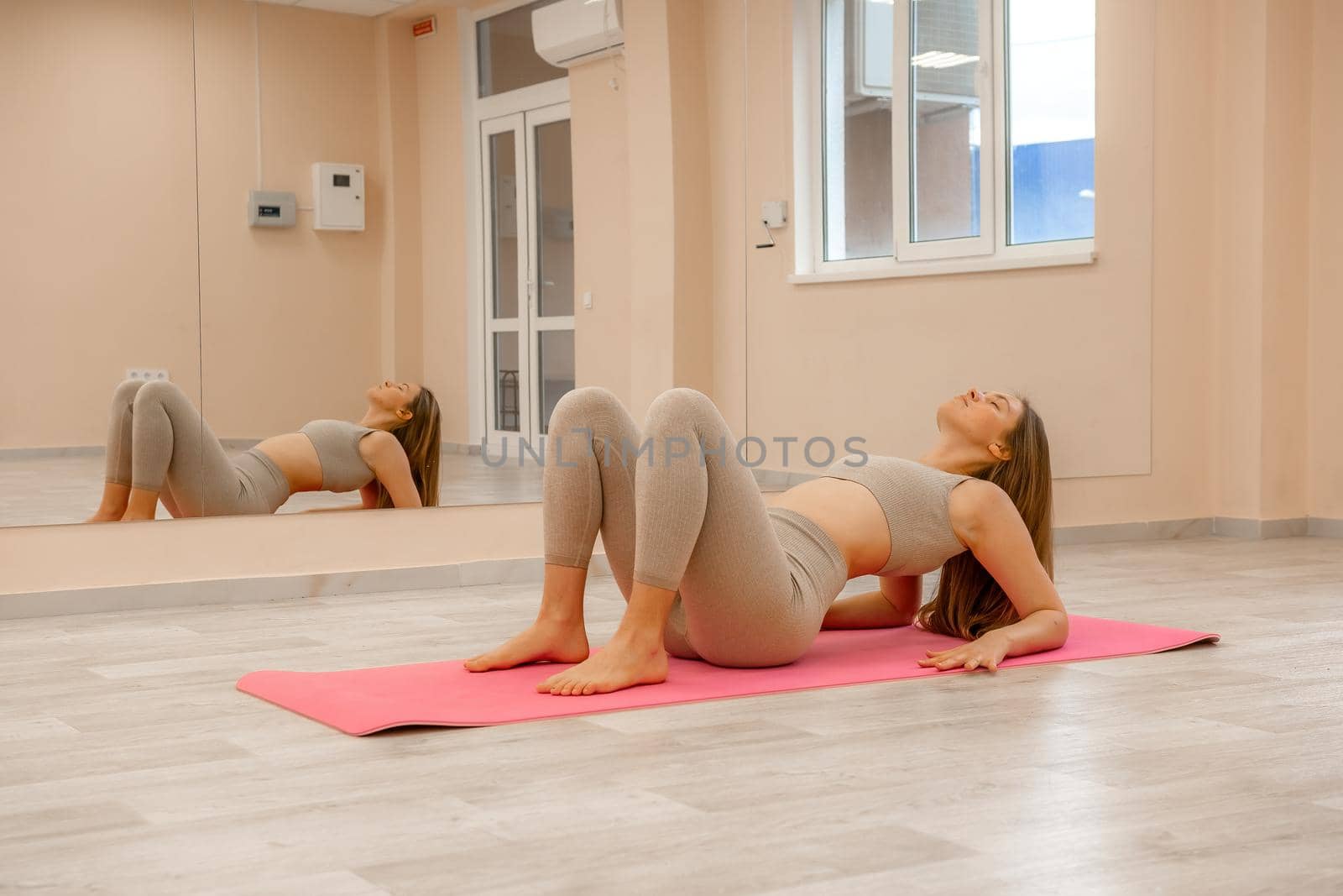 Group of young womans fitness instructor in Sportswear Leggings and Tops, stretching in the gym before pilates, on a yoga mat near the large window on a sunny day, female fitness yoga routine concept.