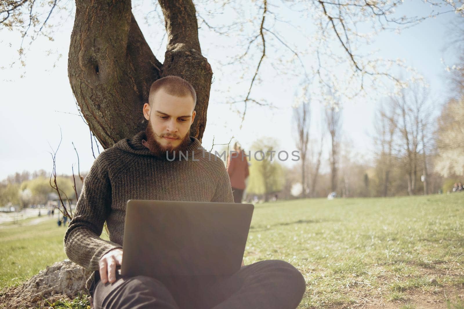 Young man using and typing laptop computer in summer grass.