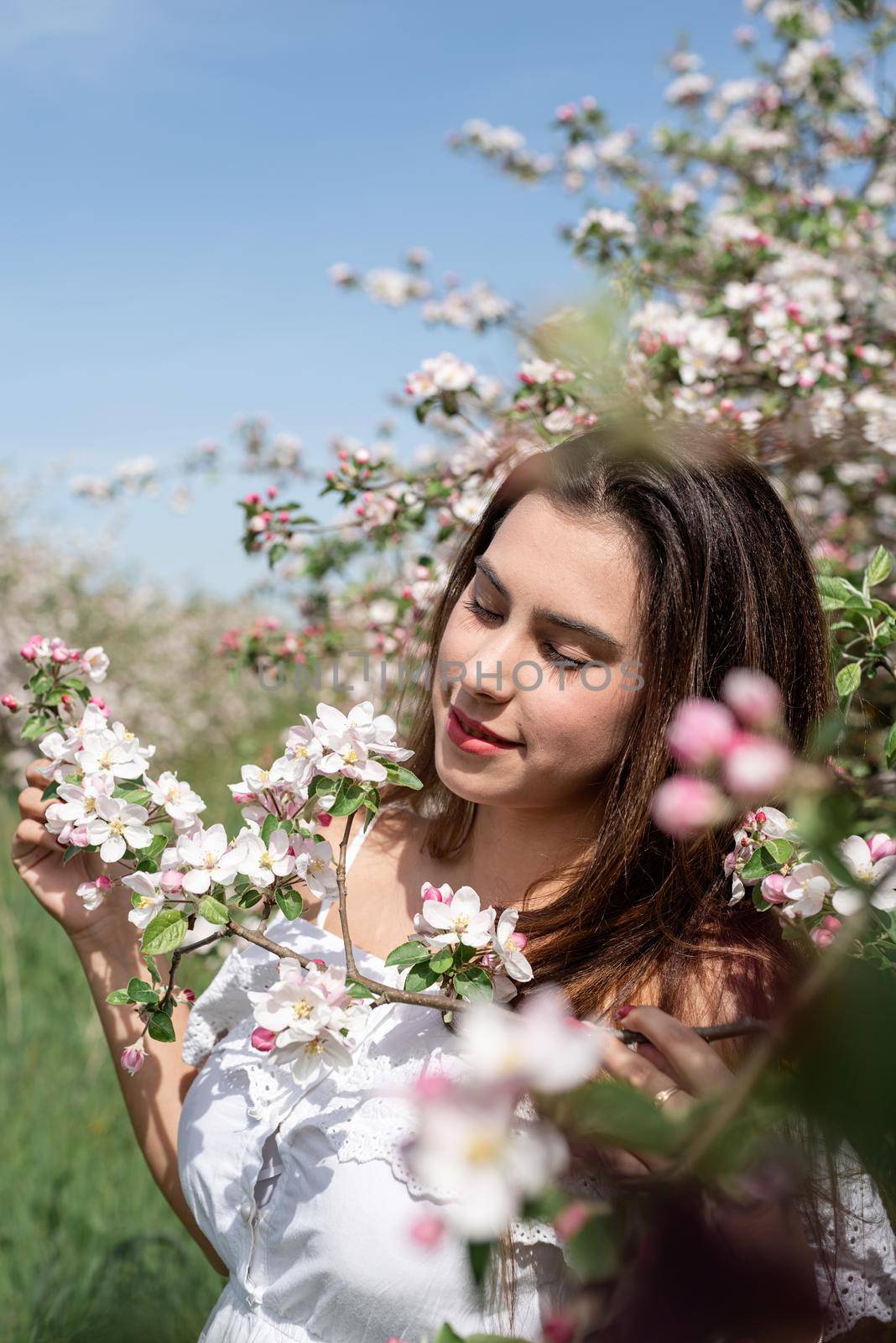 Spring concept. Nature. Young caucasian woman in white summer dress enjoying the flowering of an apple trees, walking in spring apple gardens