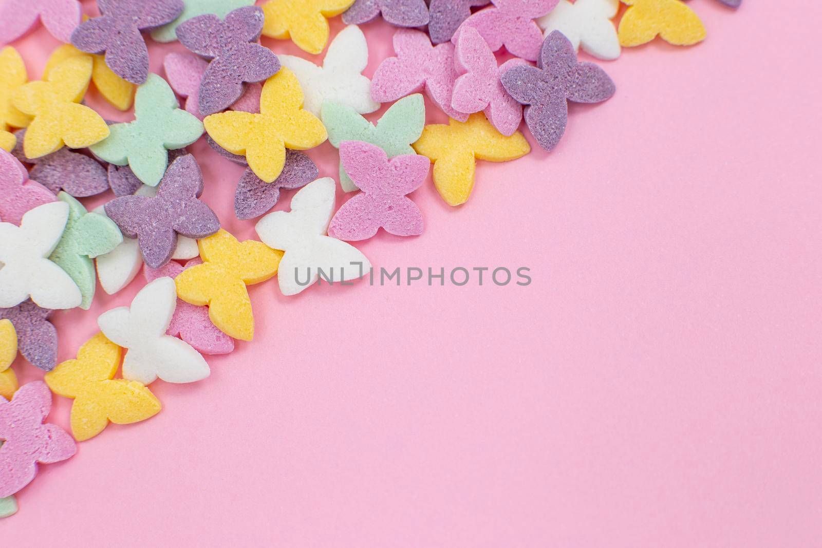 Colorful butterflies, a popular sugar confectionery topping, lie on a pink background diagonally in the left corner. Close-up. Top view. Copy space