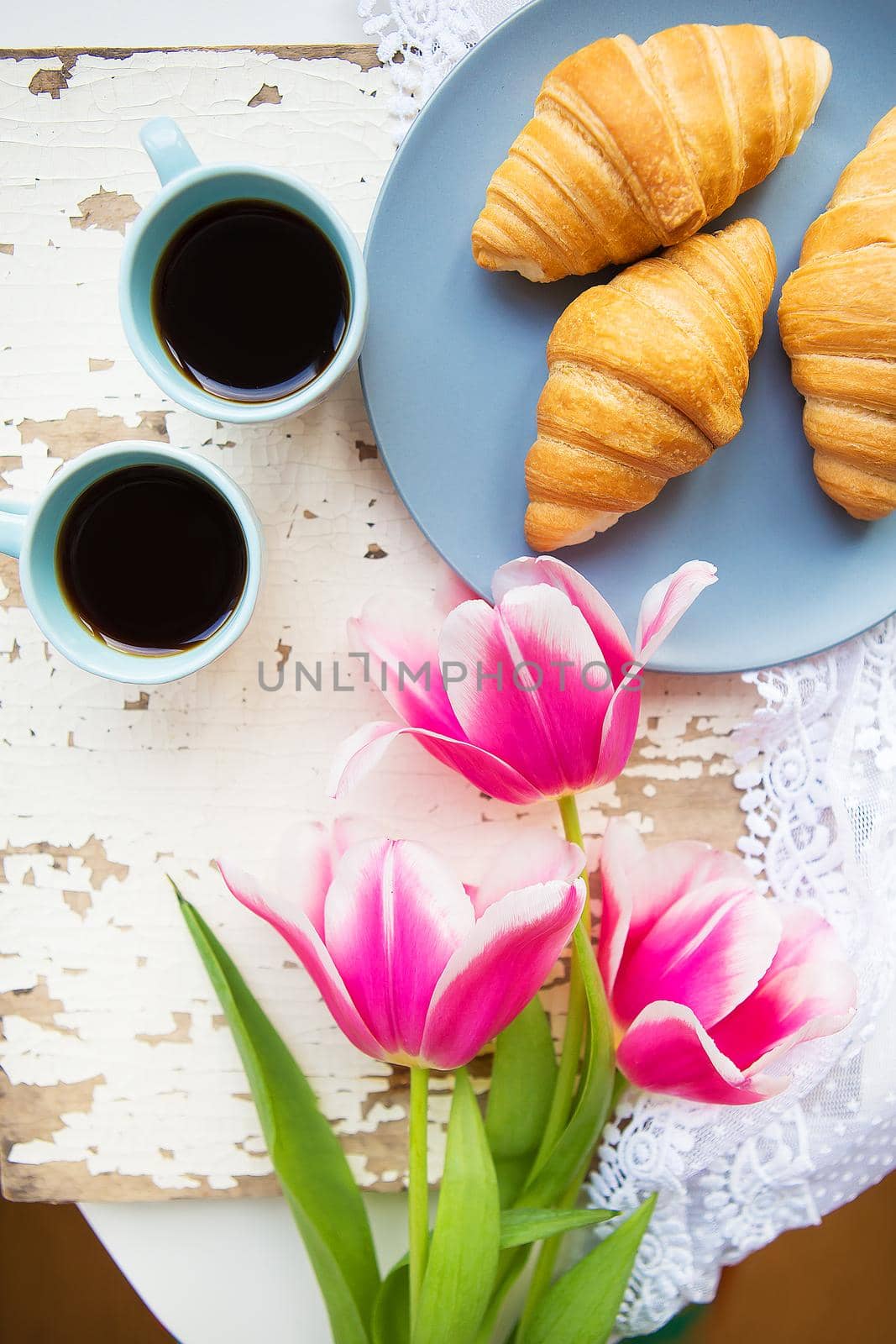 coffee, croissants and three beautiful pink tulips on old white table.