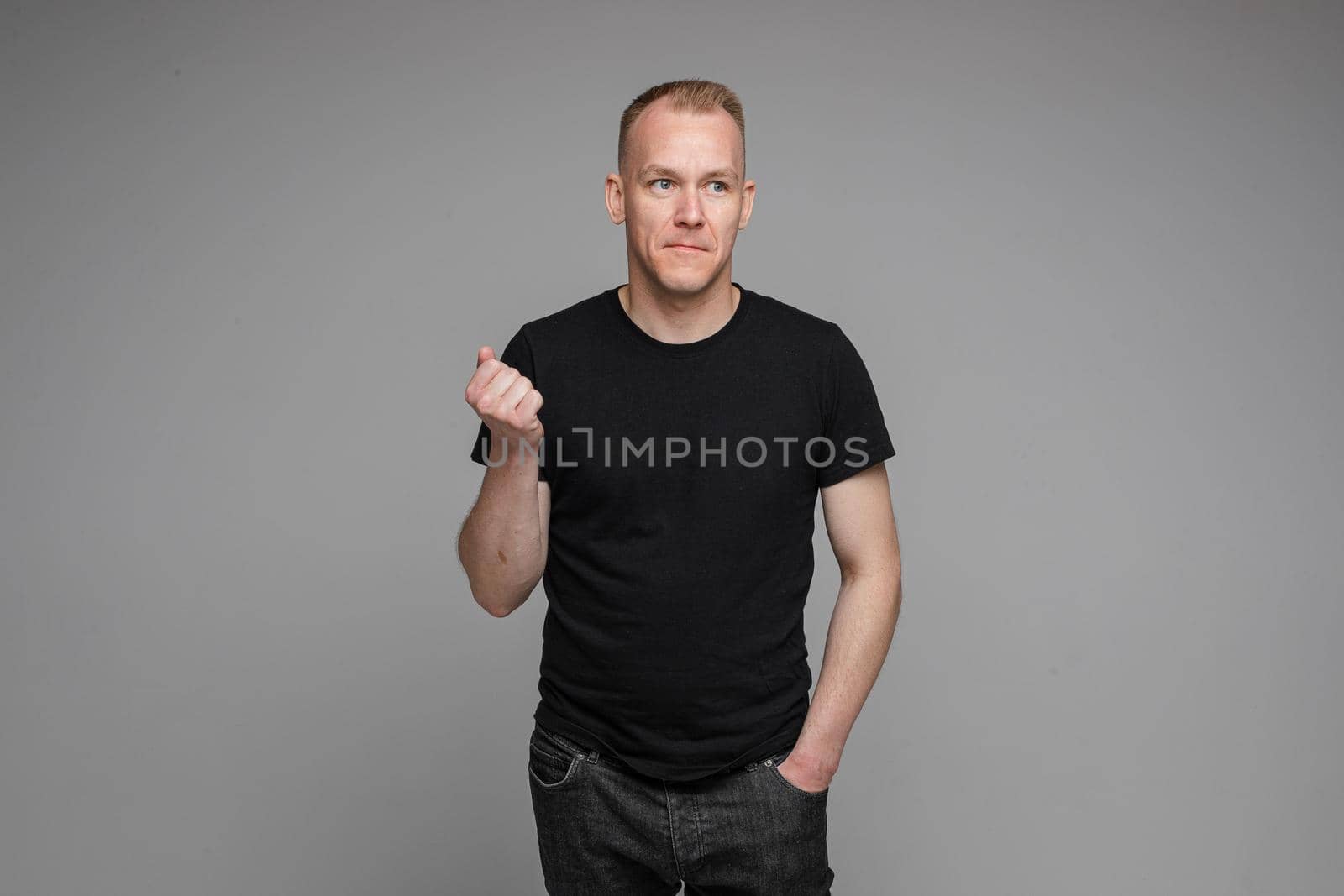 picture of caucasian man keeps his hands in the pockets of his black jeans and looks to the right isolated on grey background