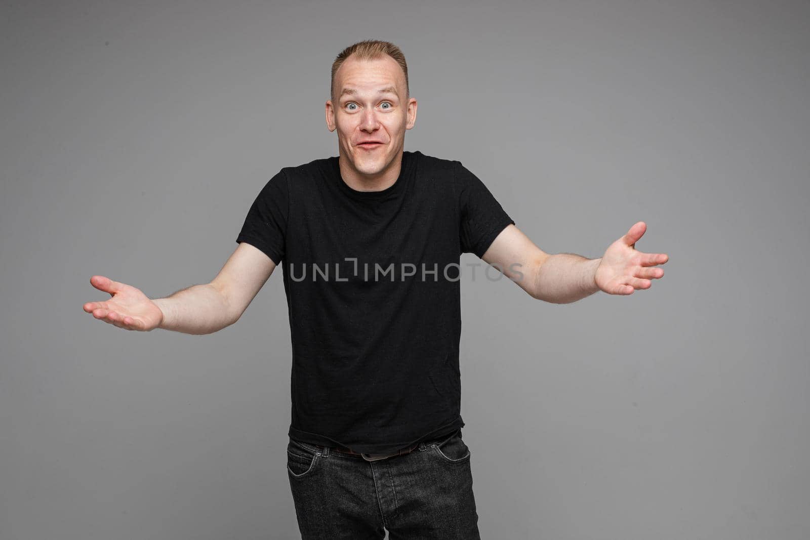 picture of caucasian man keeps his hands to the sides and looks to the camera isolated on grey background