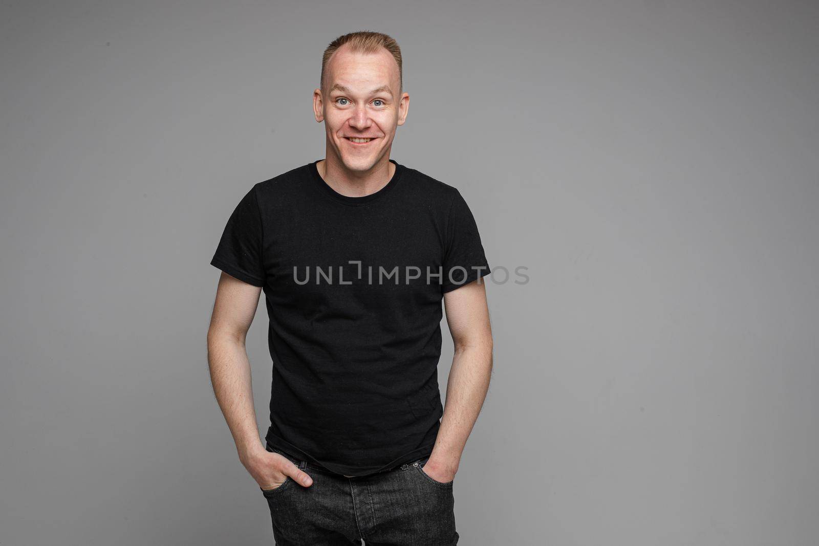 Surprised Caucasian man in black looking at camera with smile with hands on his waist.