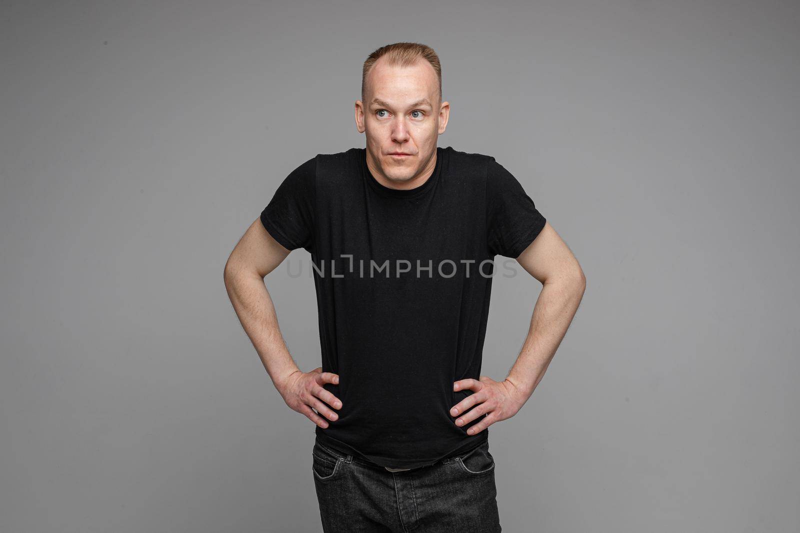 Surprised Caucasian man in black looking at camera with smile with hands on his waist.