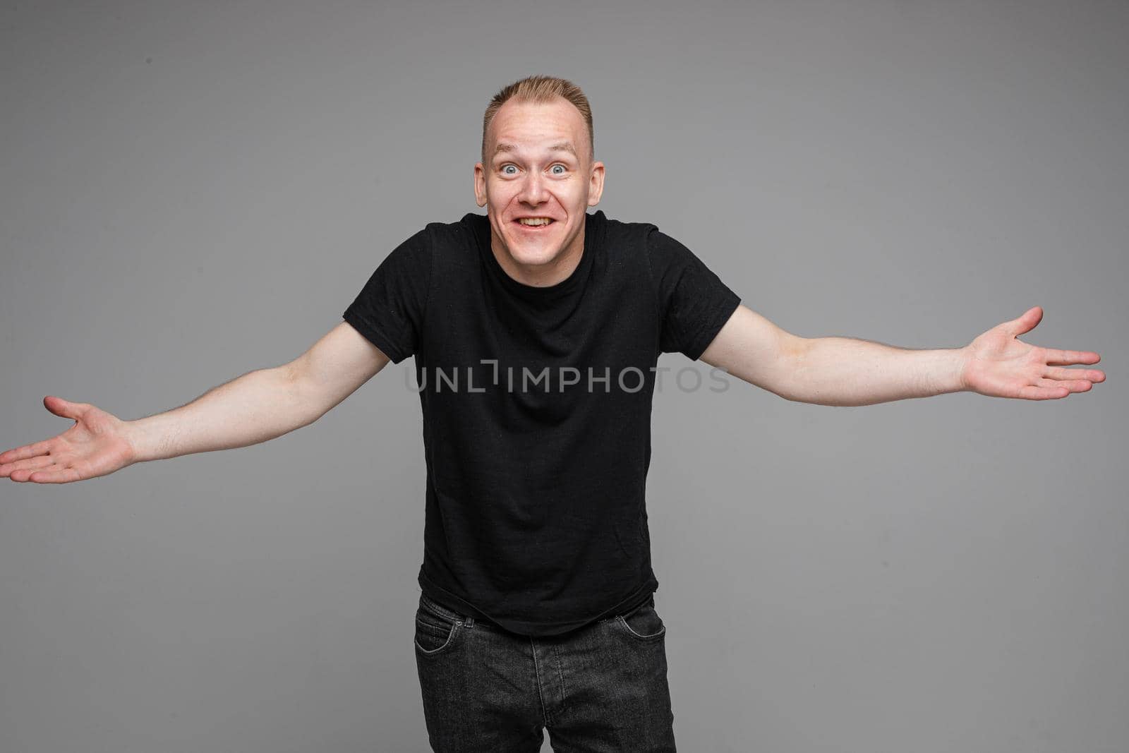 picture of caucasian man keeps his hands to the sides and looks to the camera isolated on grey background