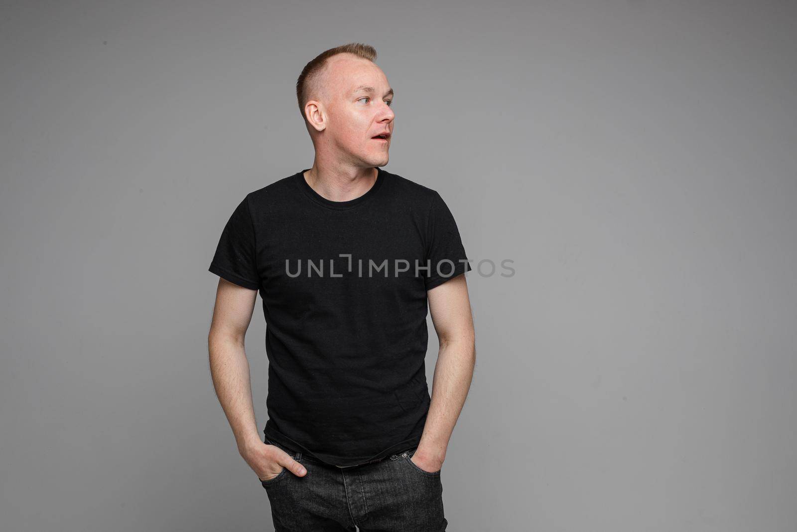 Surprised Caucasian man in black looking at camera with smile with hands on his waist.