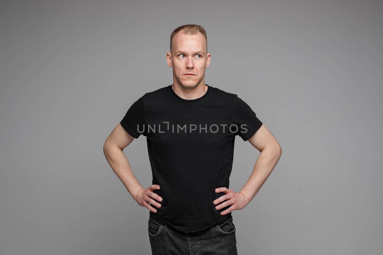 Surprised Caucasian man in black looking at camera with smile with hands on his waist.
