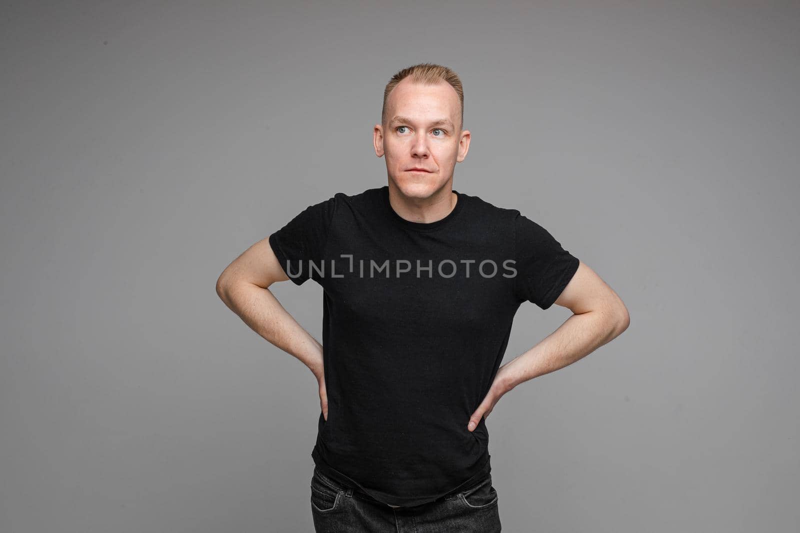 picture of handsome caucasian male keeps his hands on the belt and looks aside isolated on grey background