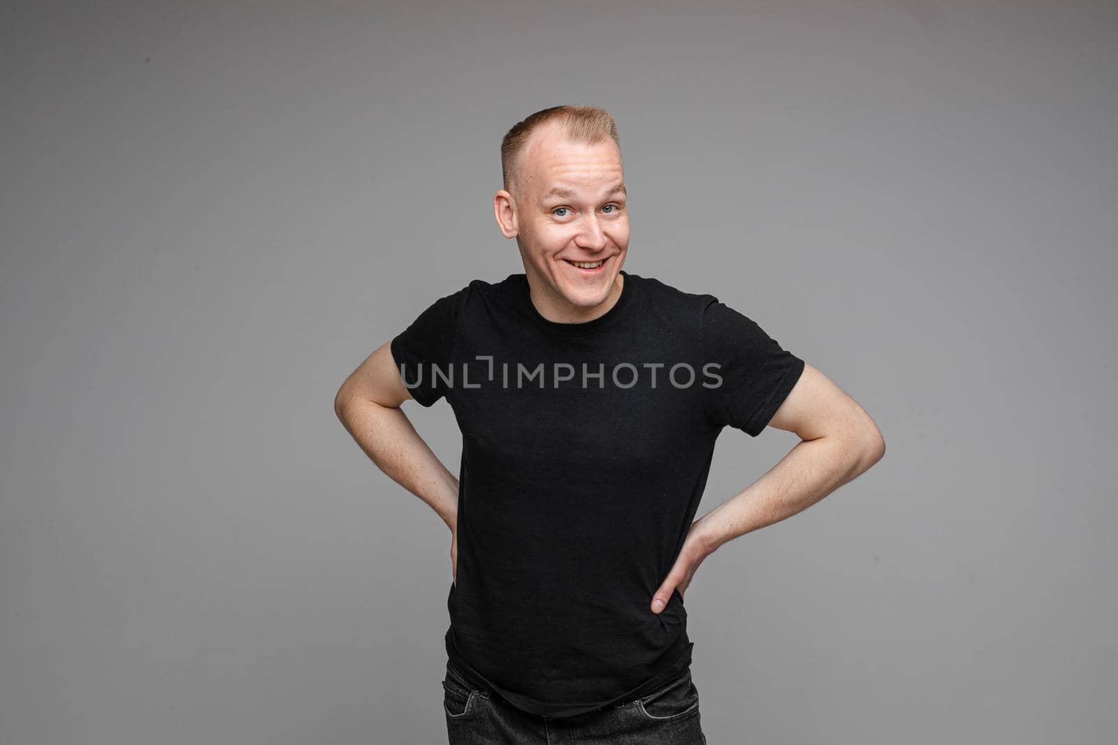 picture of handsome caucasian male keeps his hands on the belt and looks aside isolated on grey background