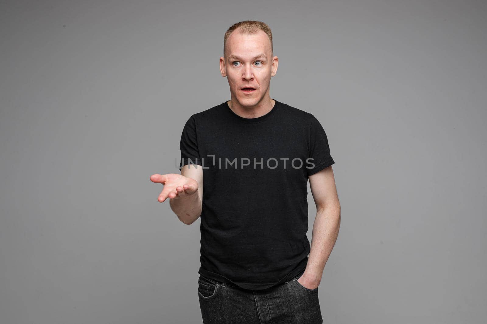 picture of handsome caucasian male keeps hands together looks with surprised sight isolated on grey background