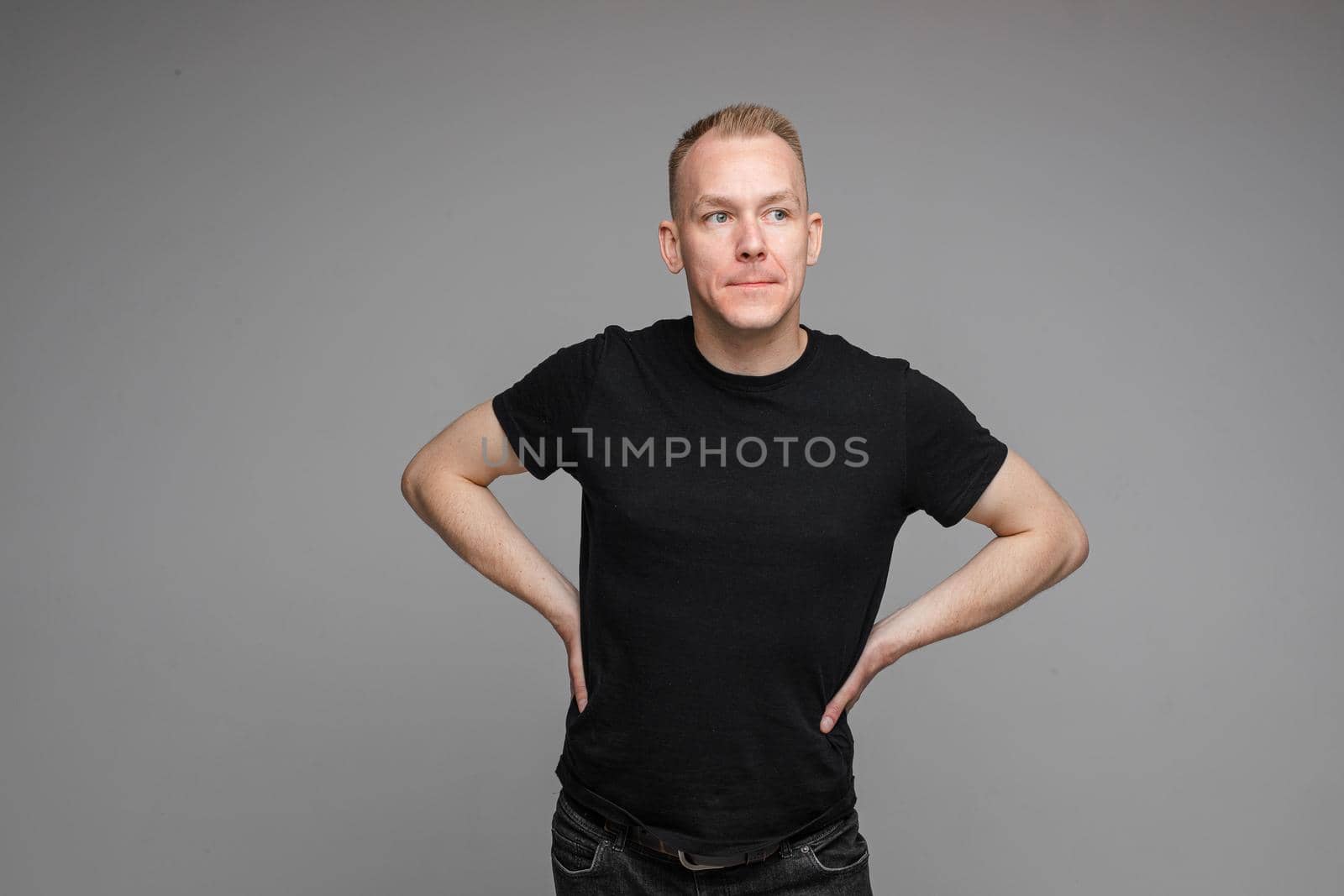picture of handsome caucasian male keeps his hands on the belt and looks aside isolated on grey background