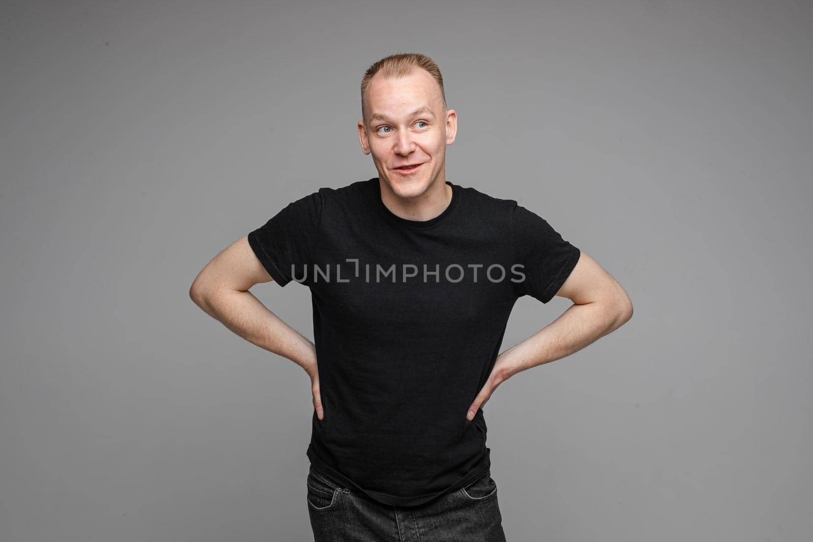 picture of handsome caucasian male keeps his hands on the belt and looks aside isolated on grey background