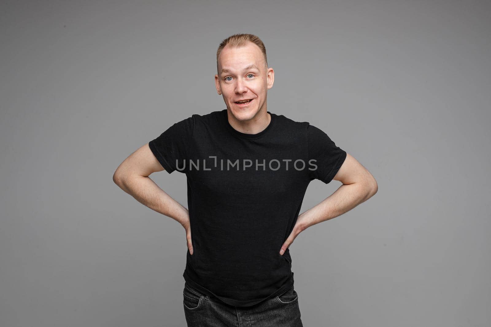 picture of handsome caucasian male keeps his hands on the belt and looks aside isolated on grey background