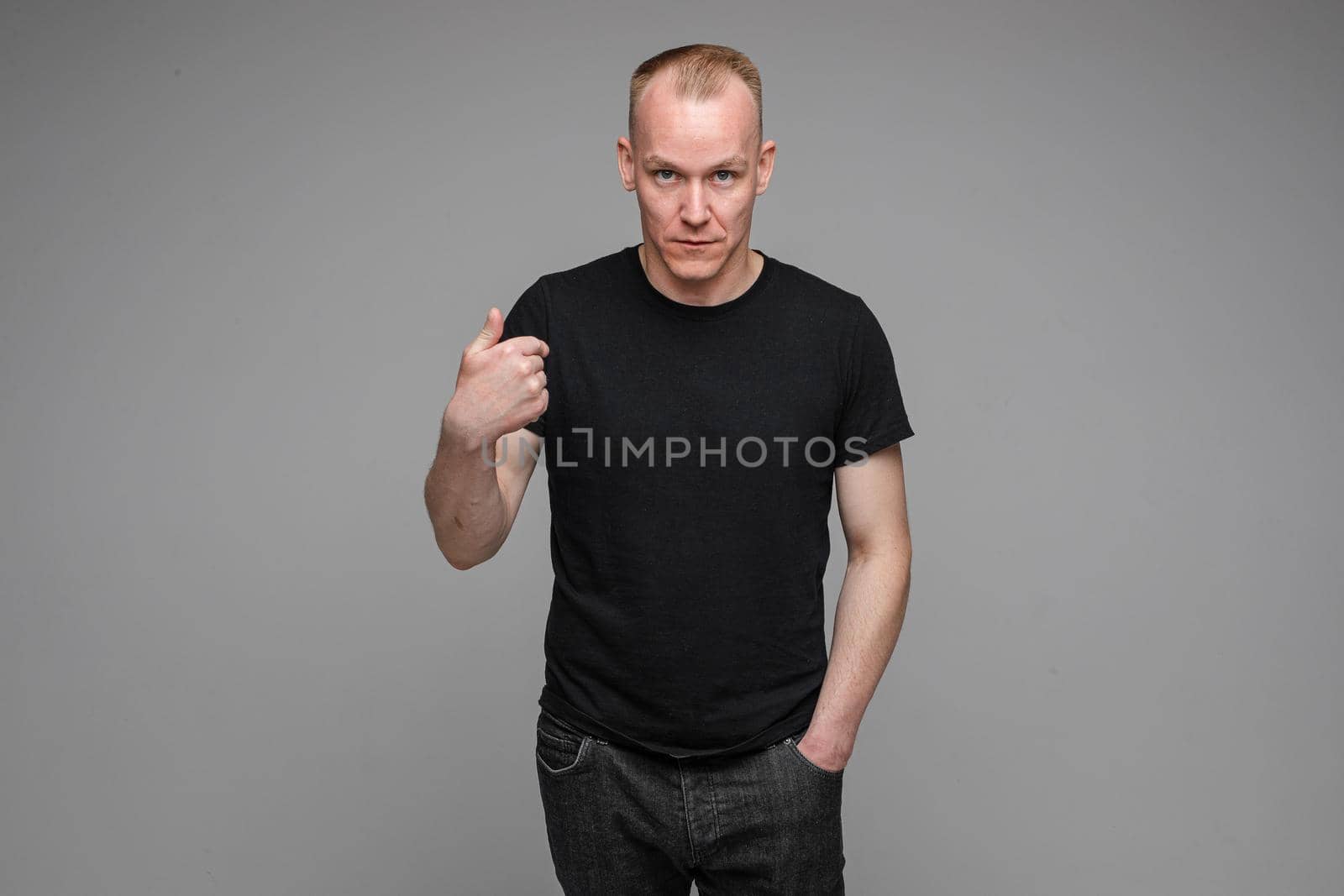 caucasian man with short fair hair wearing a black t-shirt and jeans points to himself with a finger by StudioLucky