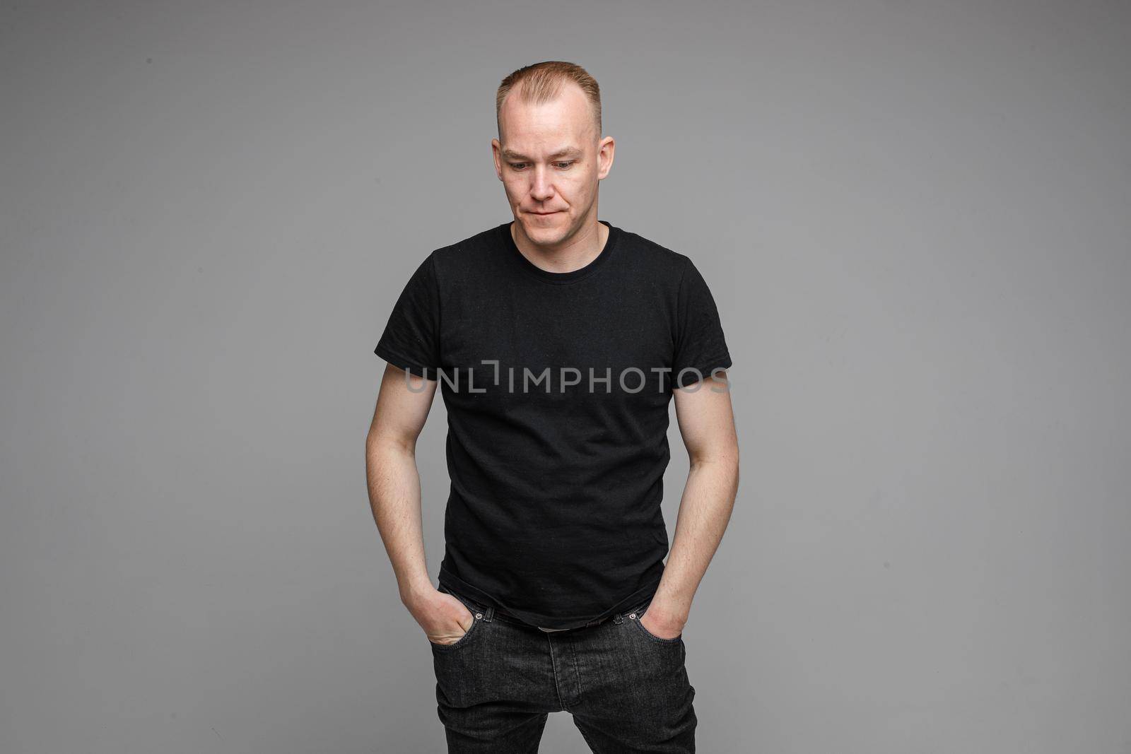Portrait of Caucasian blond man in black clothing showing disbelief shrugging his shoulders and pointing at camera with his hand asking what is the problem.