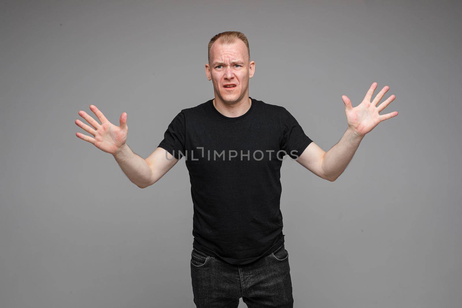 Portrait of dissatisfied angry blond Caucasian man in black holding his arms outstretched showing disapproval and asking to stop it.