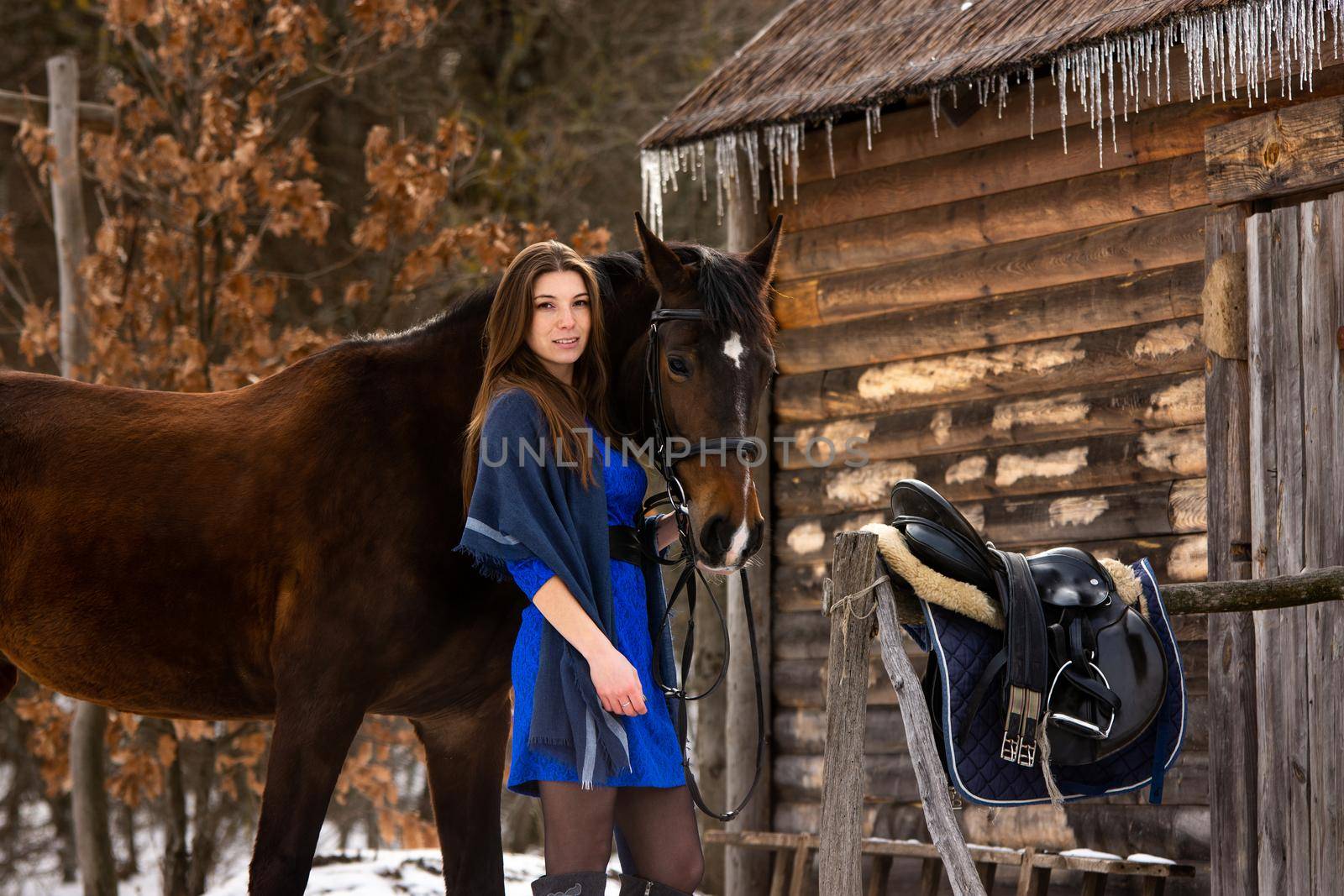 A beautiful girl in a short blue dress stands with a horse against the background of old ruins