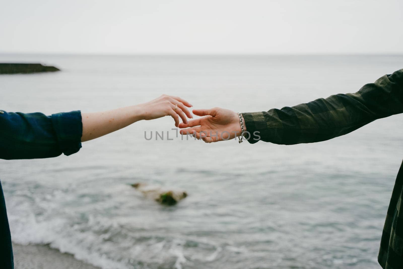 Couple stretches their arms to each other over the sea. Spring or summer holidays. The concept of family. Natural landscape. The hand of a girl and a guy reach out to each other on the seashore.